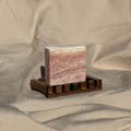 sea salt rosemary exfoliating soap bar on wooden soap dish against neutral fabric background