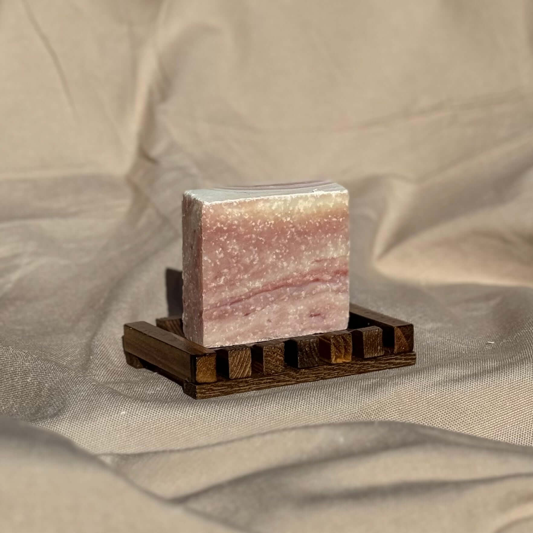 sea salt rosemary exfoliating soap bar on wooden soap dish against neutral fabric background