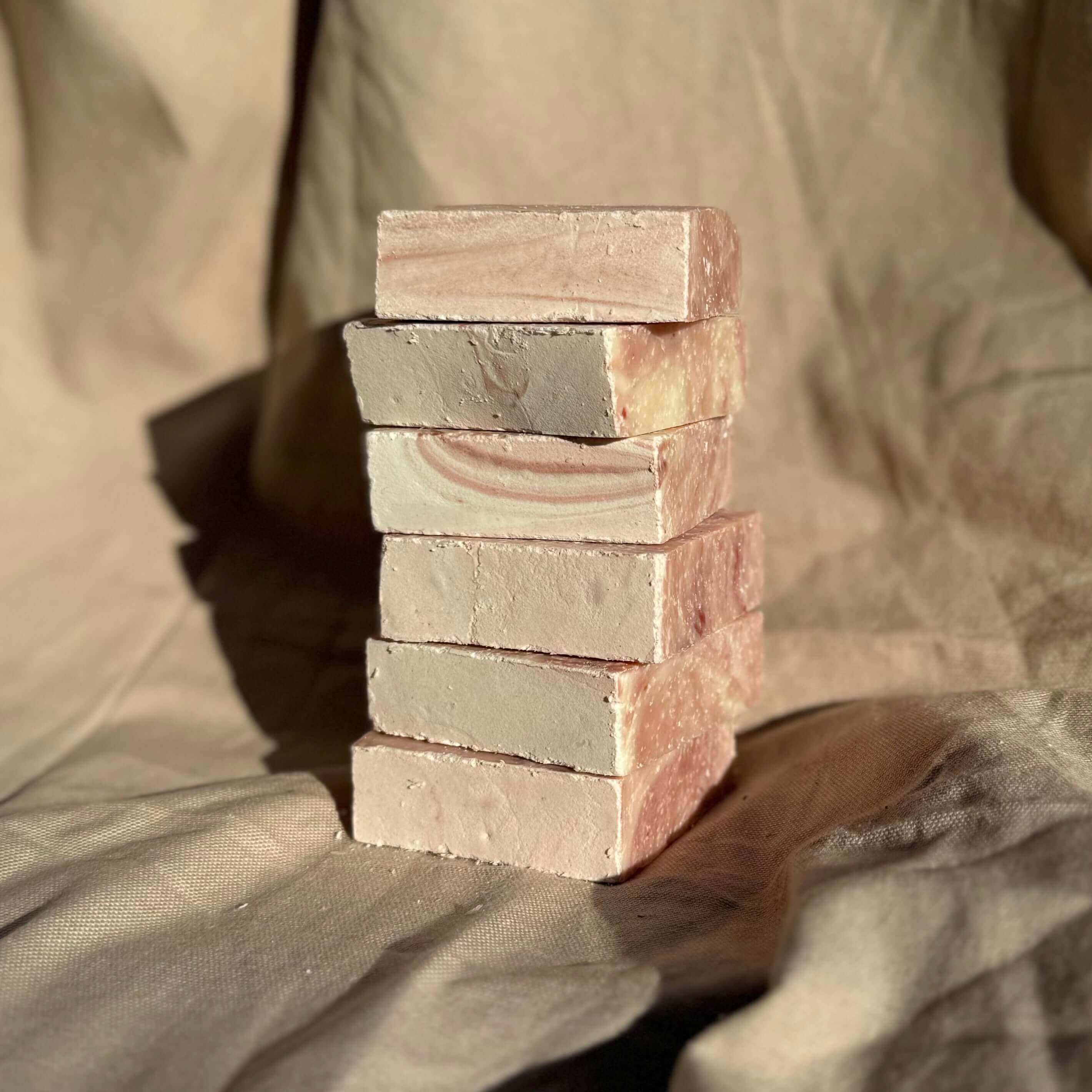 Stack of handmade sea salt rosemary exfoliating soap bar blocks on neutral fabric background