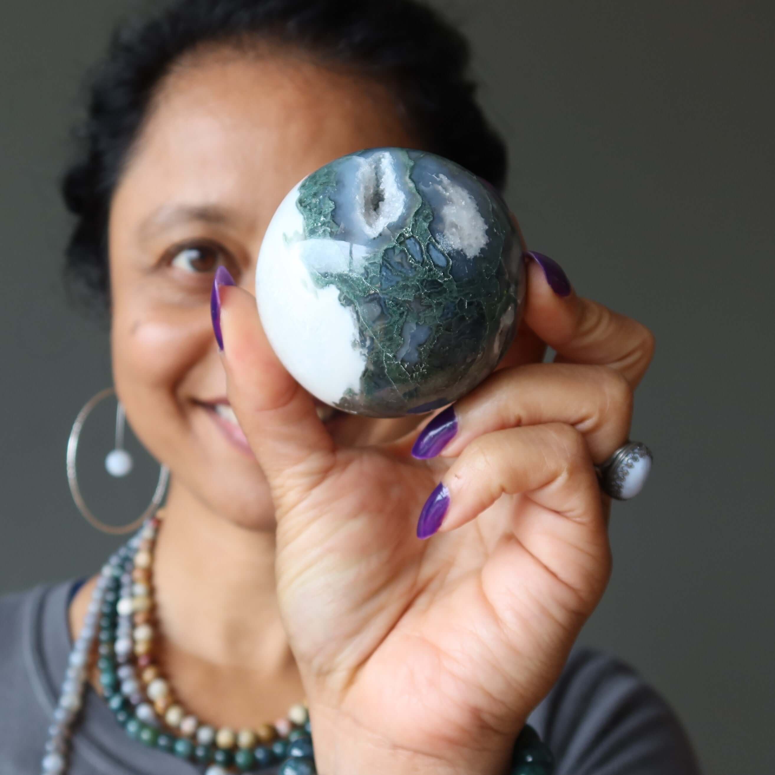 Woman holding Moss Agate sphere crystal ball with green cave-like patterns for meditation and spiritual healing