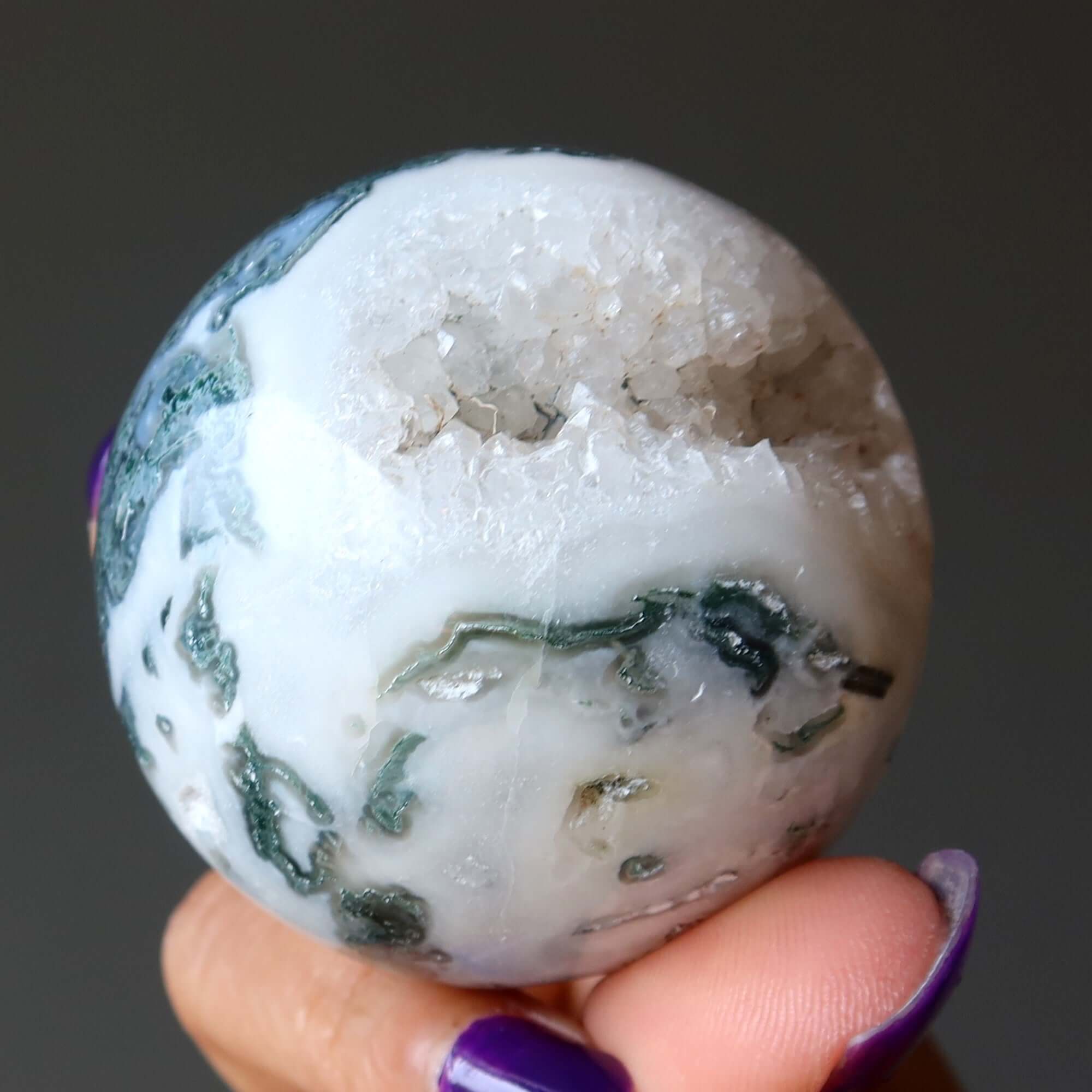 Moss Agate sphere crystal ball with white caverns and green Moss inclusions held in hand