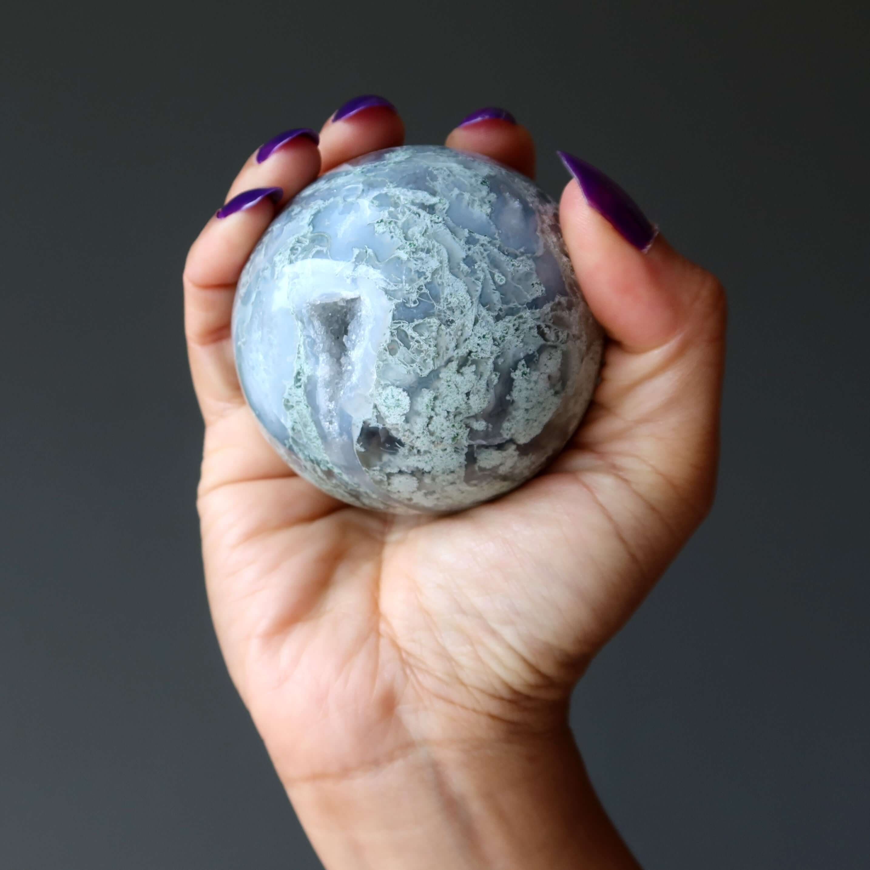 hand holding Moss Agate sphere green jungle cave crystal ball for meditation and spiritual grounding