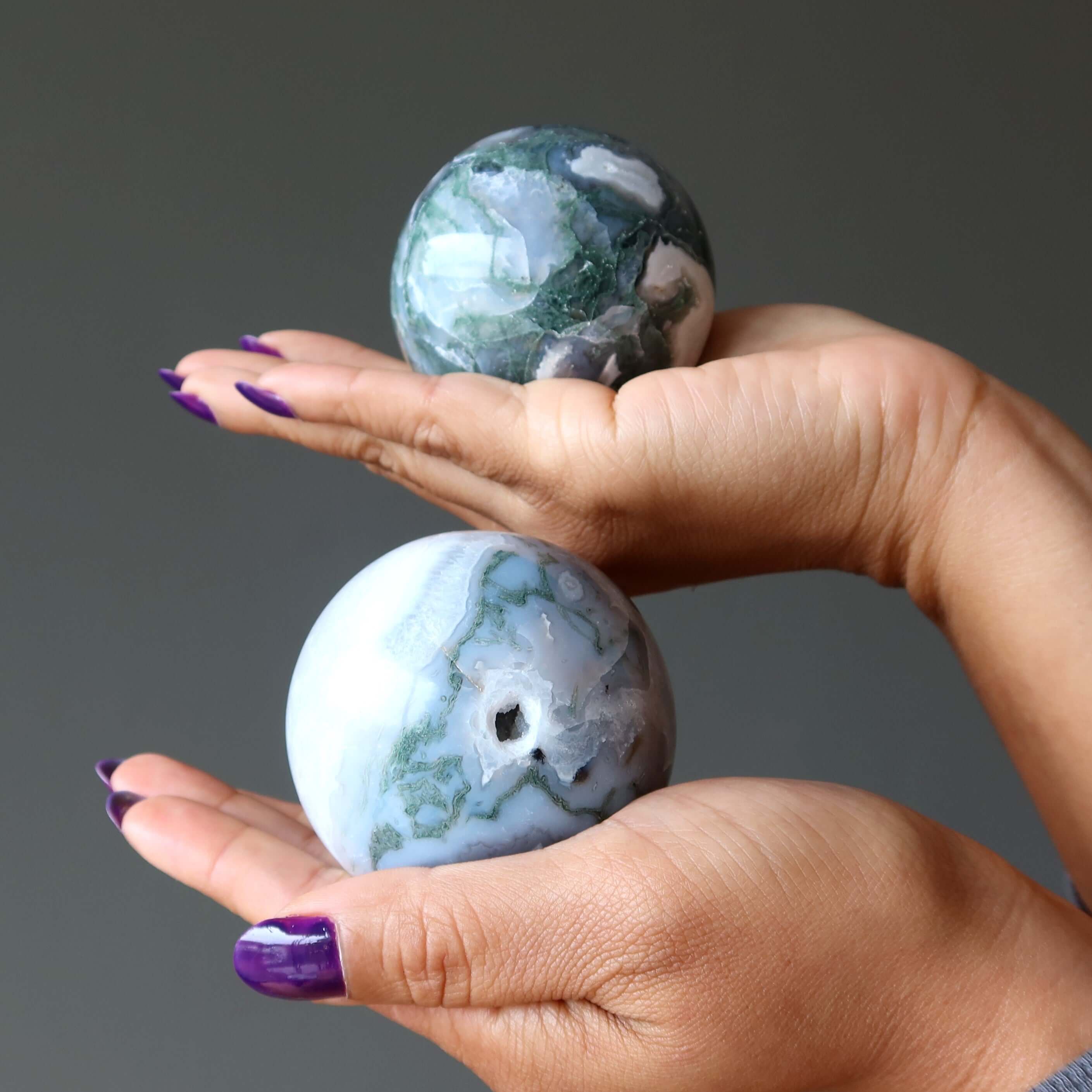 Hands holding two Moss Agate Sphere Green Jungle Cave Crystal Ball stones for meditation and spiritual healing