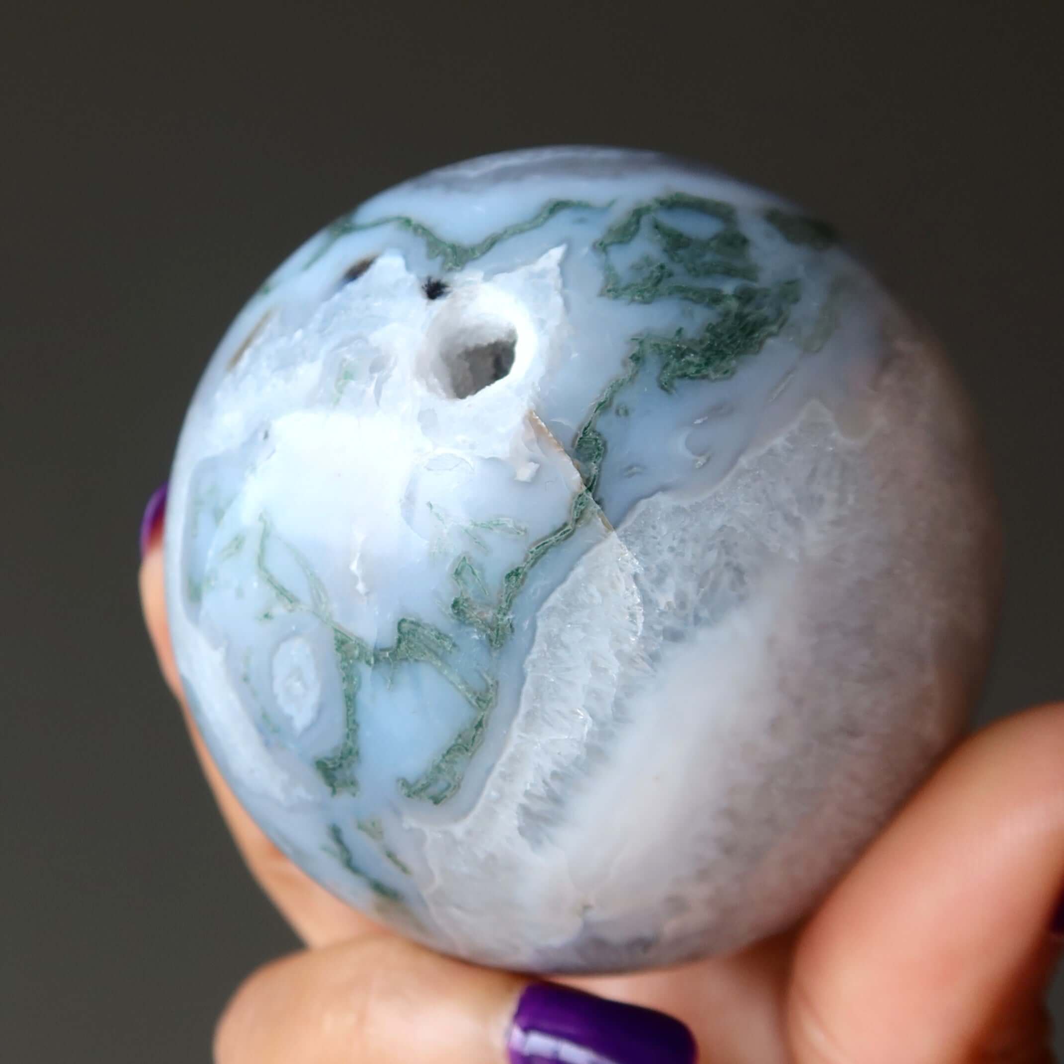 Moss agate sphere crystal ball with green moss patterns held in hand