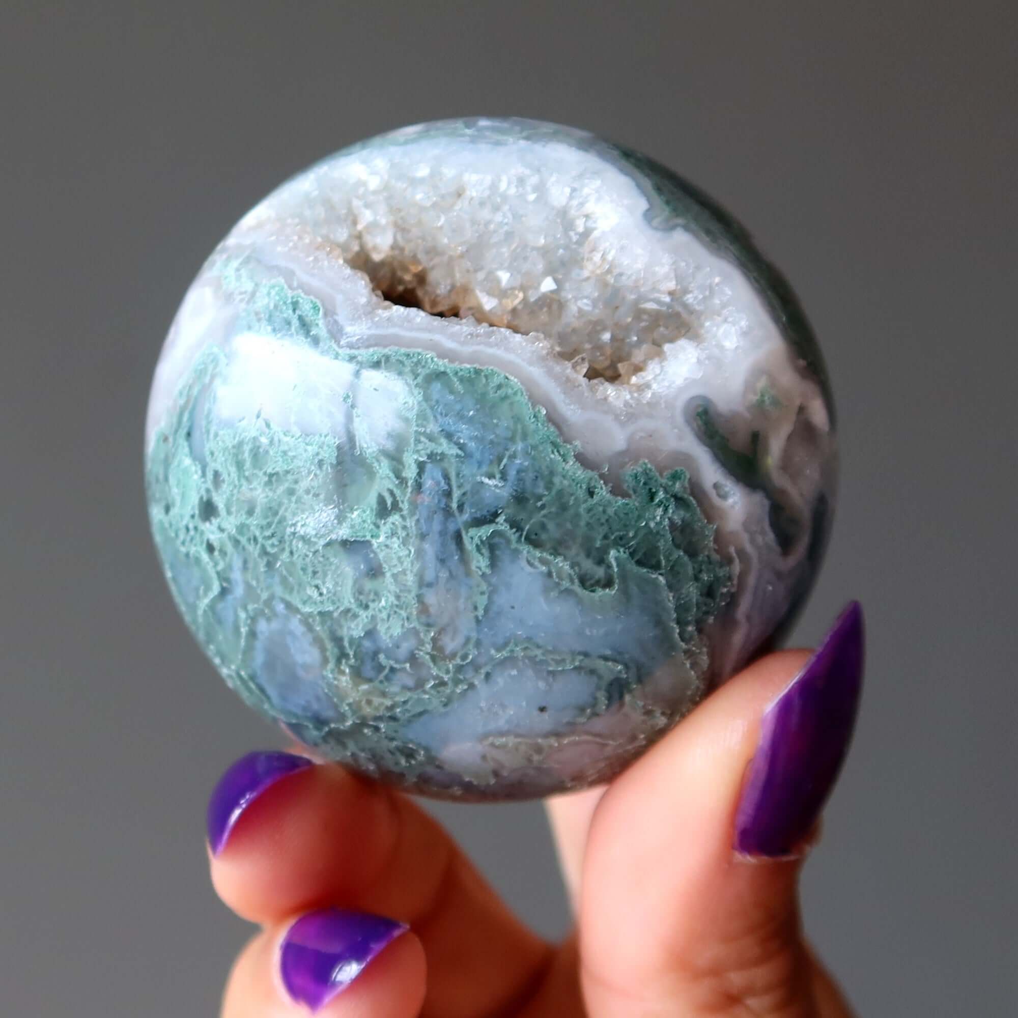 Hand holding Moss Agate Sphere Green Jungle Cave Crystal Ball with natural druzy cavern