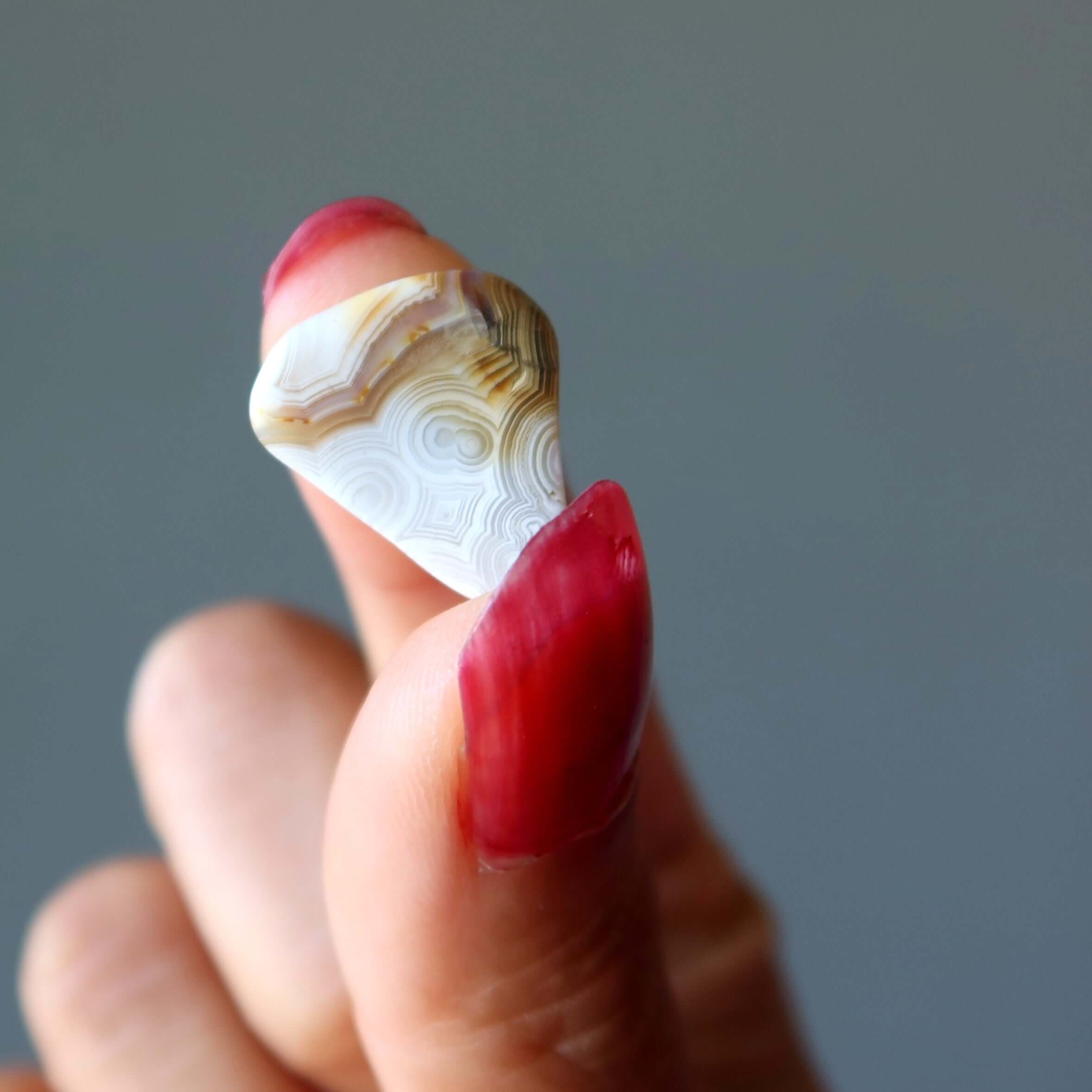 Hand holding polished lace agate tumbled stone, colorful banded crystal for grounding, calming anger and easing anxiety