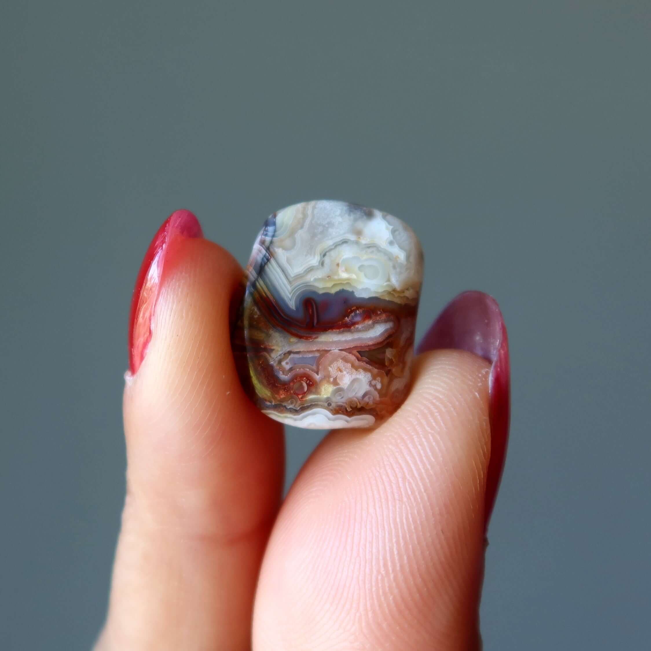 lace agate tumbled stone held between fingers, colorful banded crystal for grounding, calming anger and anxiety