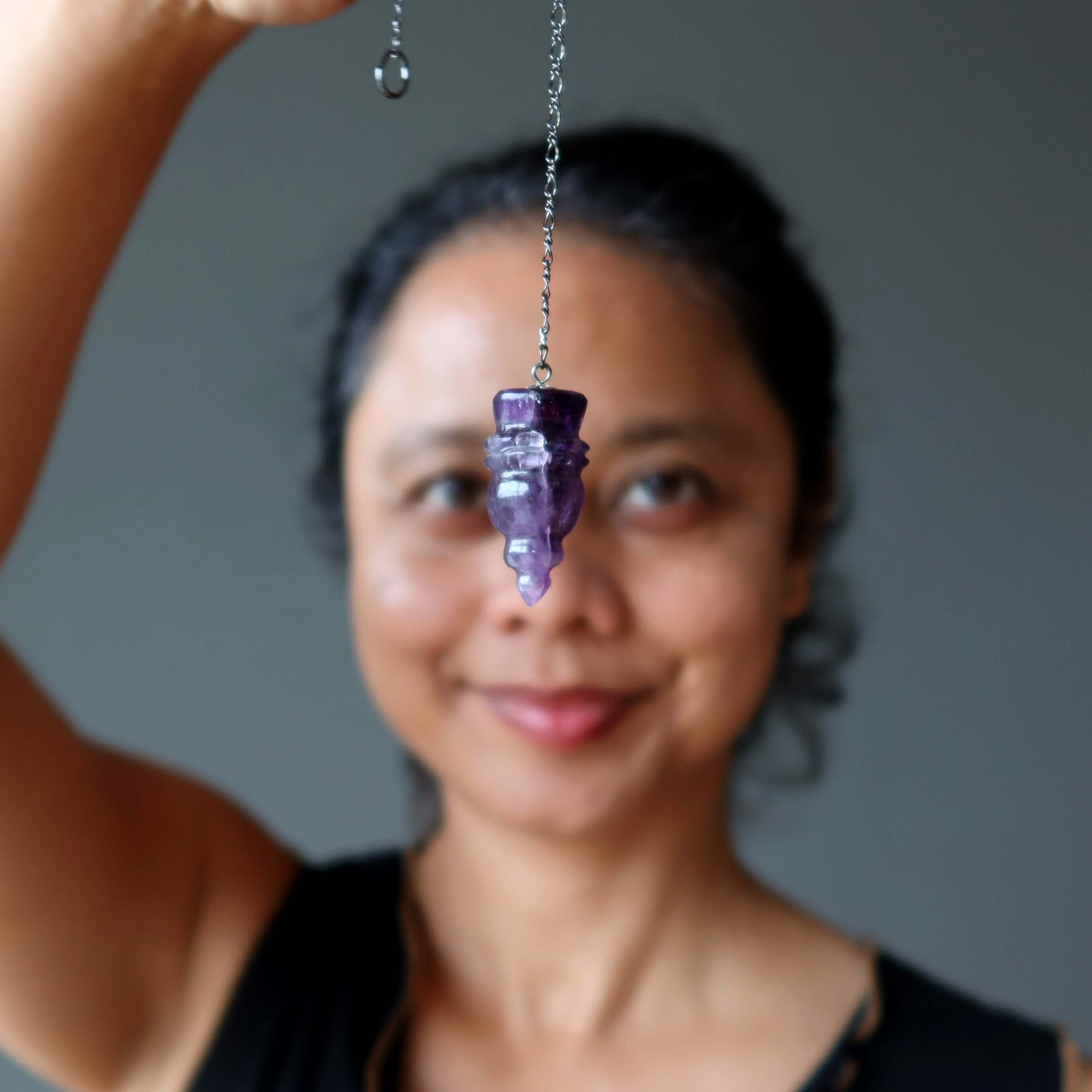 Woman holding carved crystal amethyst pendulum for dowsing, showcasing purple stone for spiritual guidance and energy work