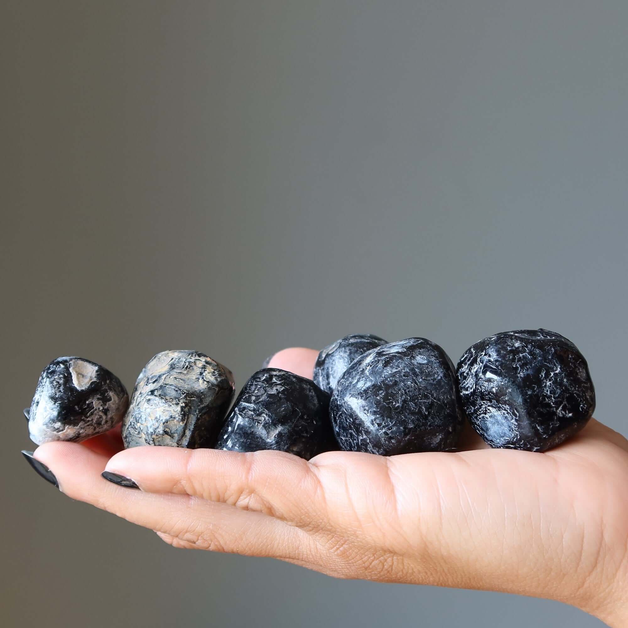 Hand holding tumbled Apache Tear obsidian mourning stones for grief healing and negative energy protection