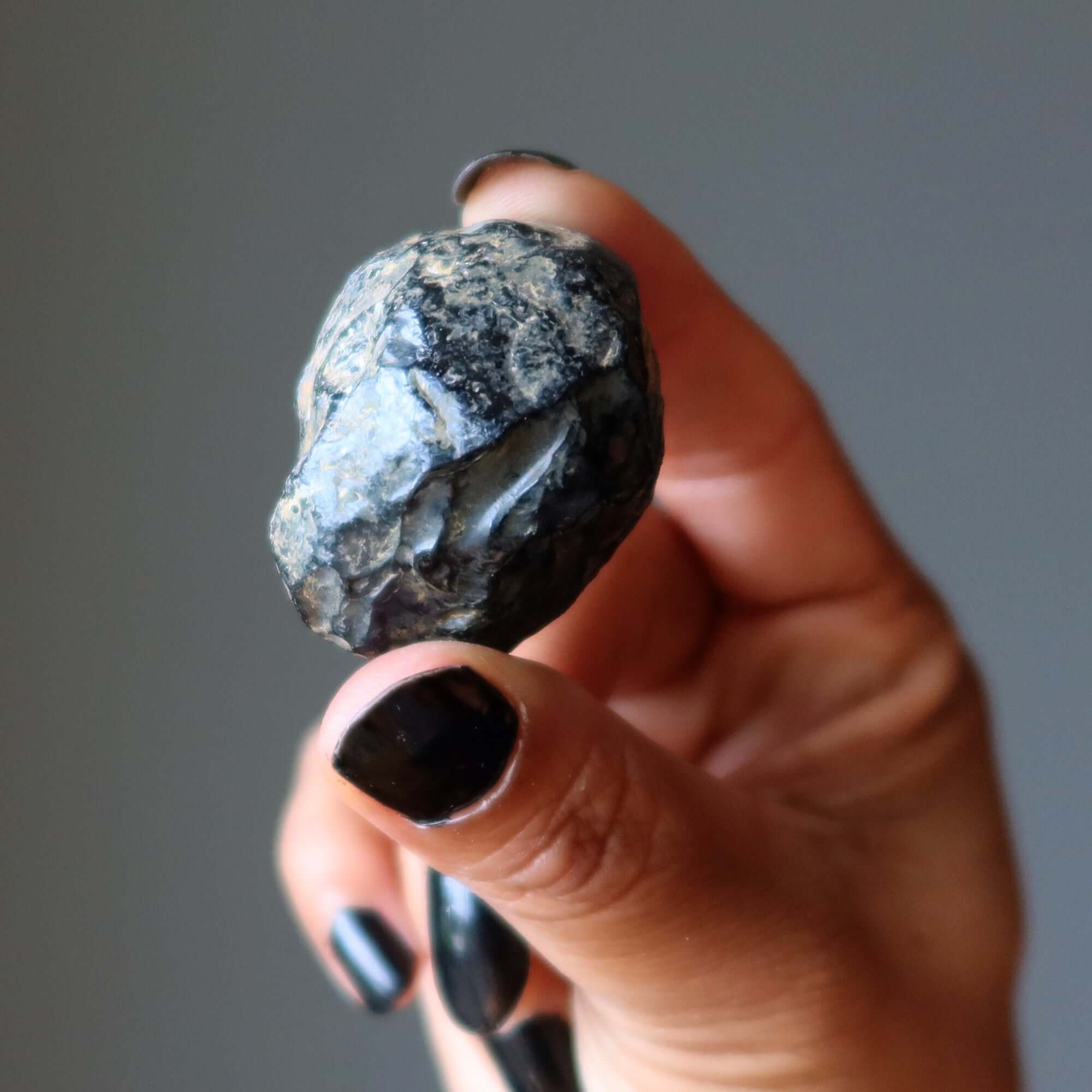 Hand holding raw Apache Tear Obsidian mourning stone crystal for grief support and negative energy protection