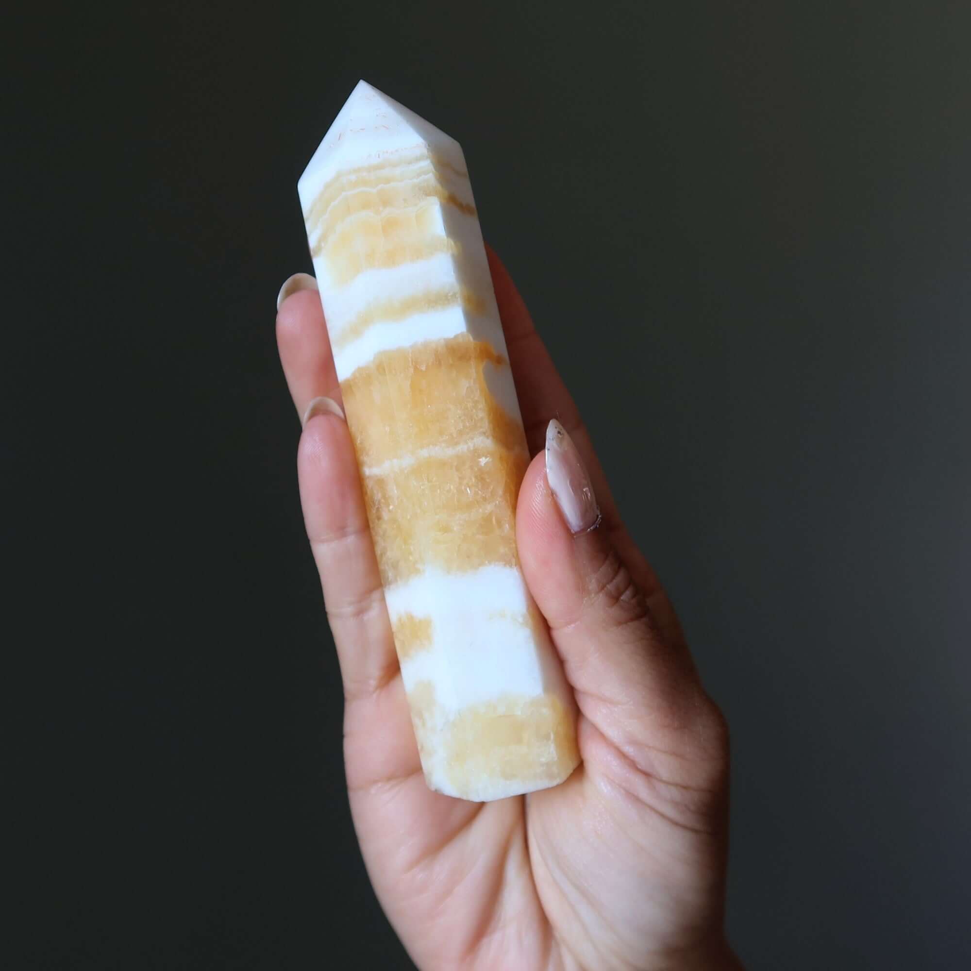 Orange calcite tower wand crystal held in hand, striped yellow and white point for confidence and solar plexus chakra energy