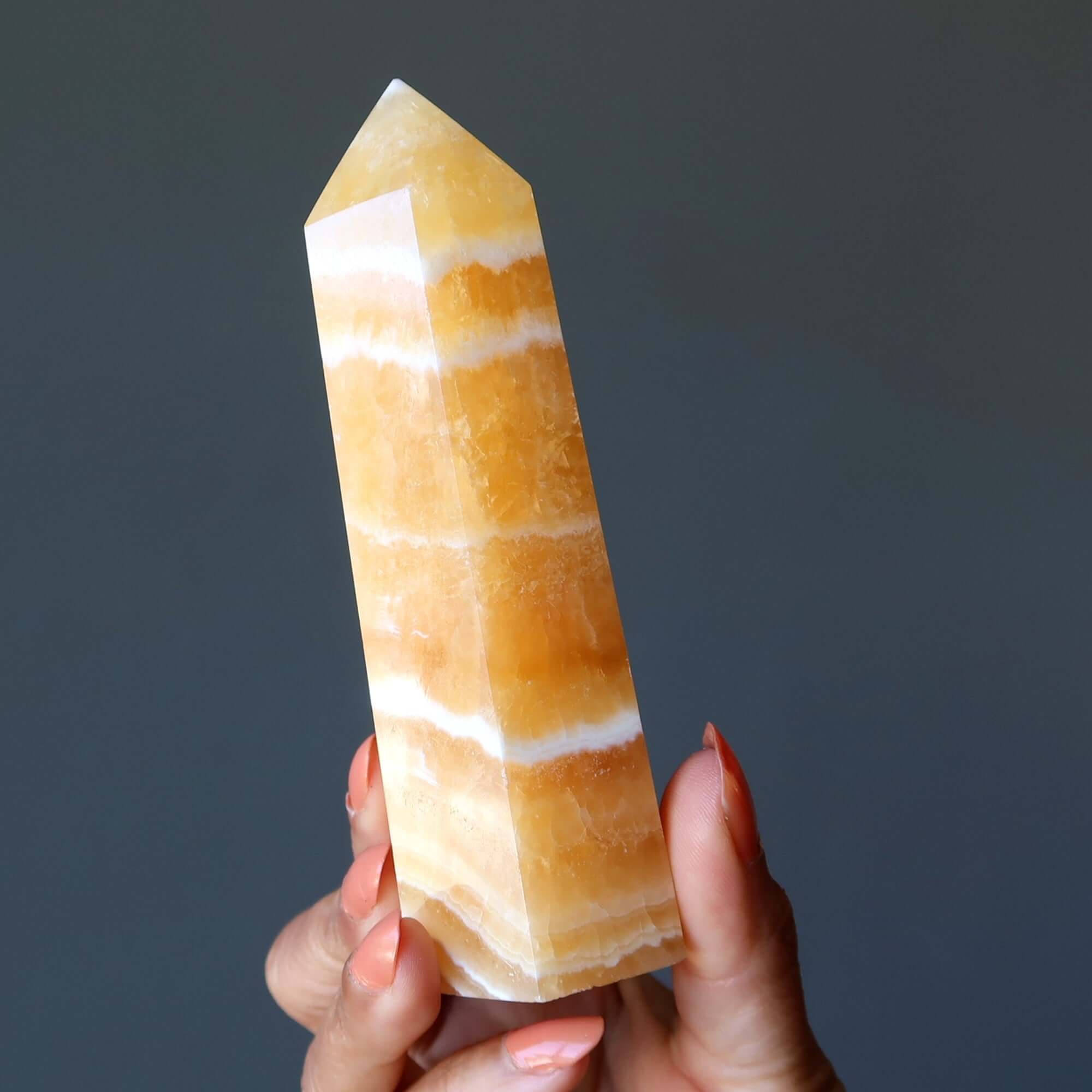 Orange calcite tower wand crystal point held in hand, confidence boosting solar plexus healing stone