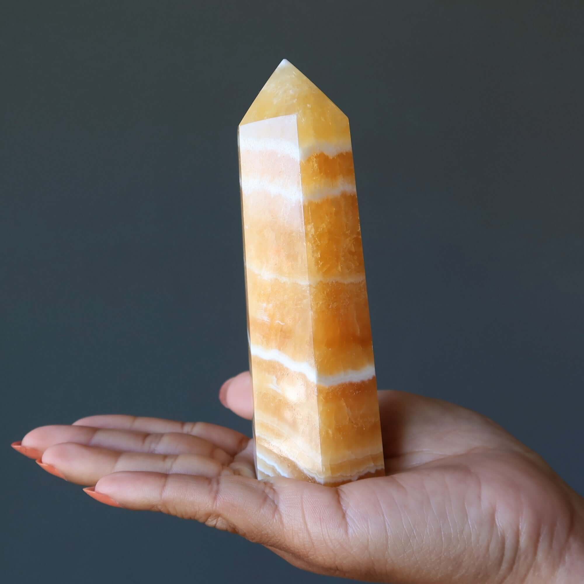 Orange Calcite tower wand crystal held in hand, beacon of confidence and Solar Plexus chakra energy