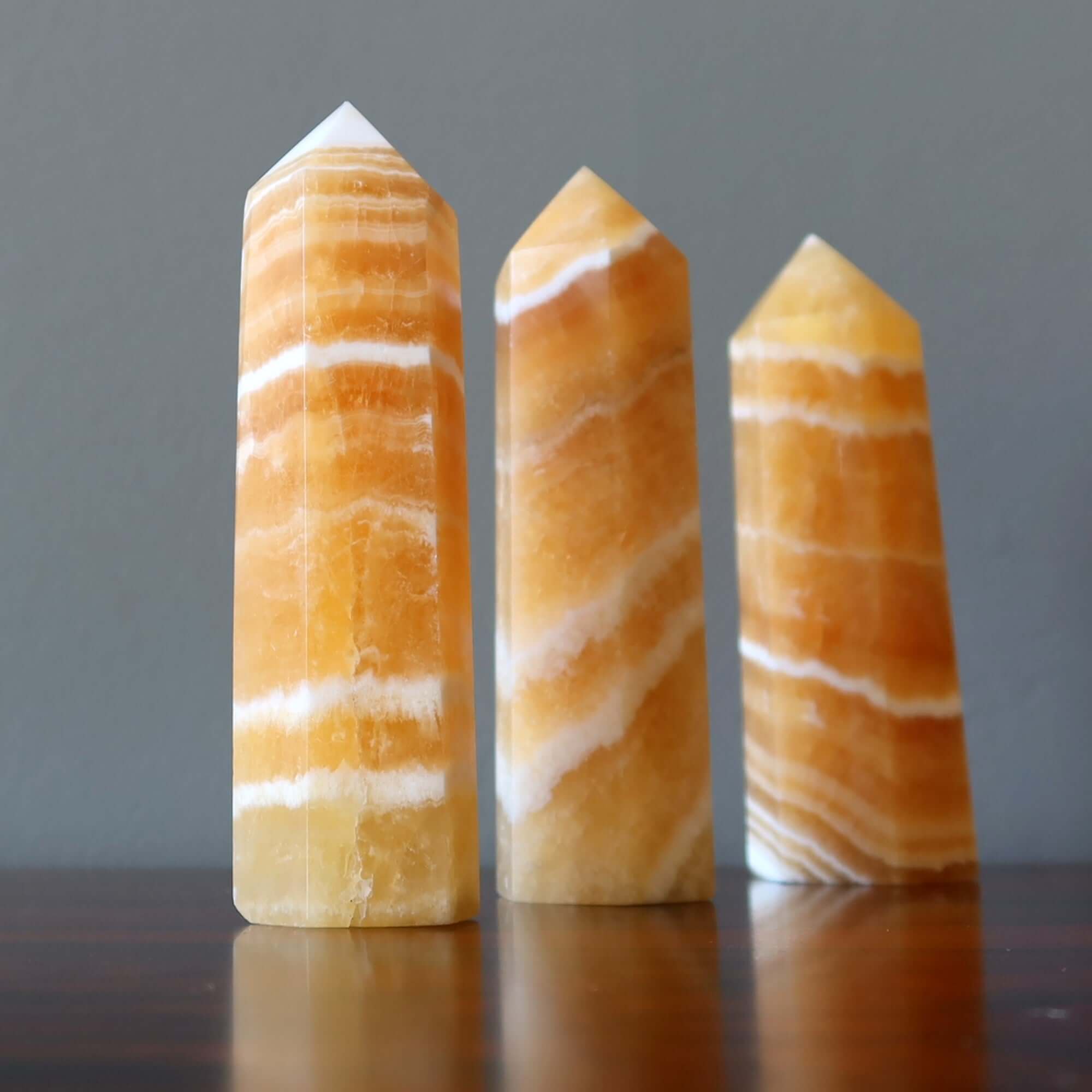 Orange Calcite tower wands crystal points for confidence and Solar Plexus chakra healing on wooden surface