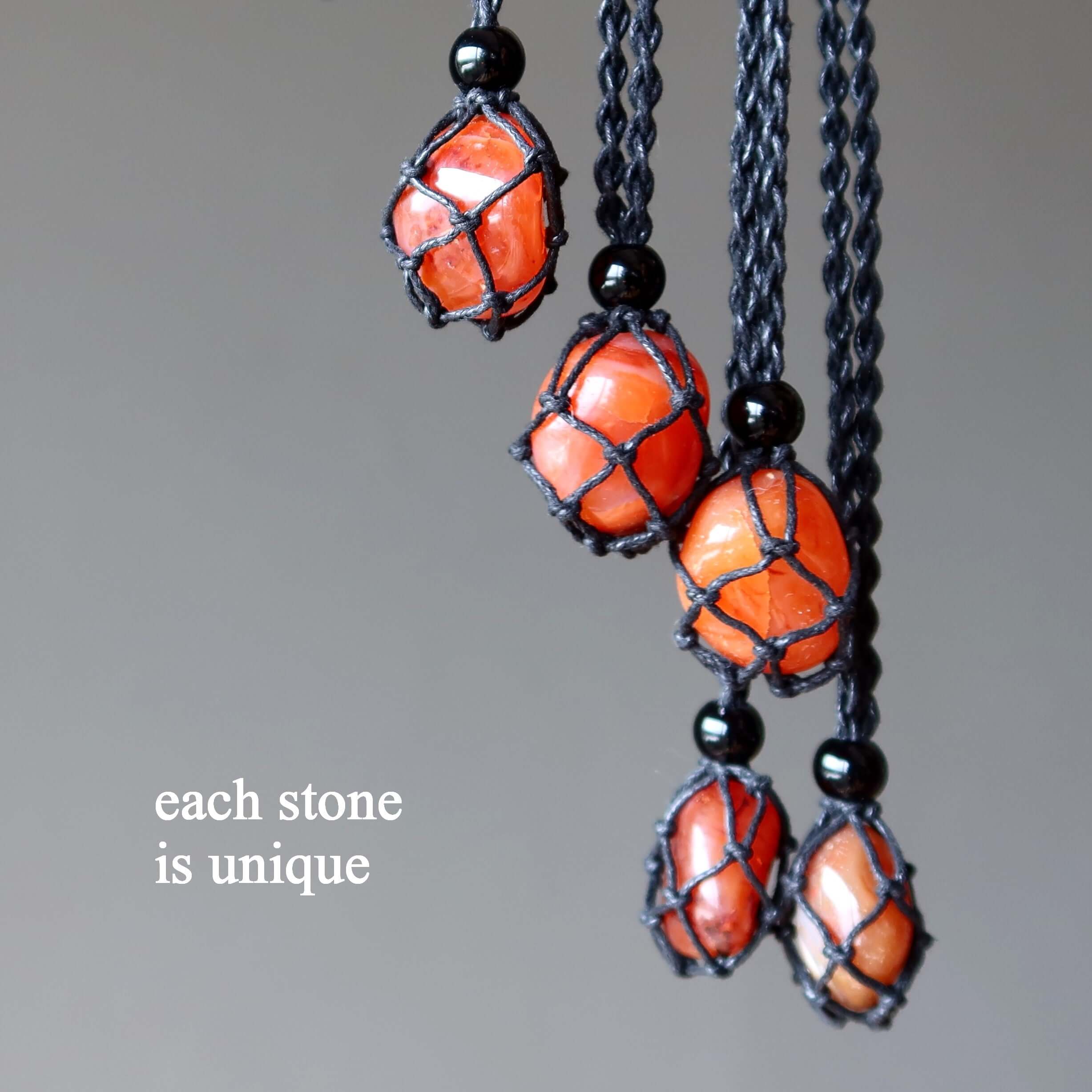 Carnelian necklace closeup with multiple orange stones in black macrame netting, each Carnelian crystal pendant shown as unique