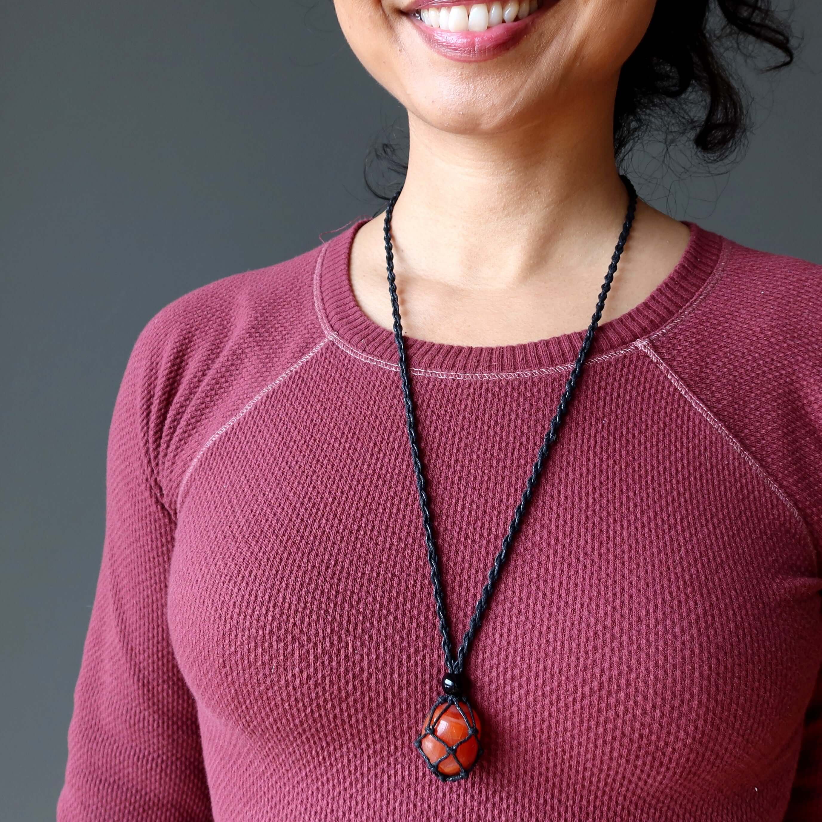Carnelian macrame necklace with orange hot stuff stone on black cord worn over maroon top
