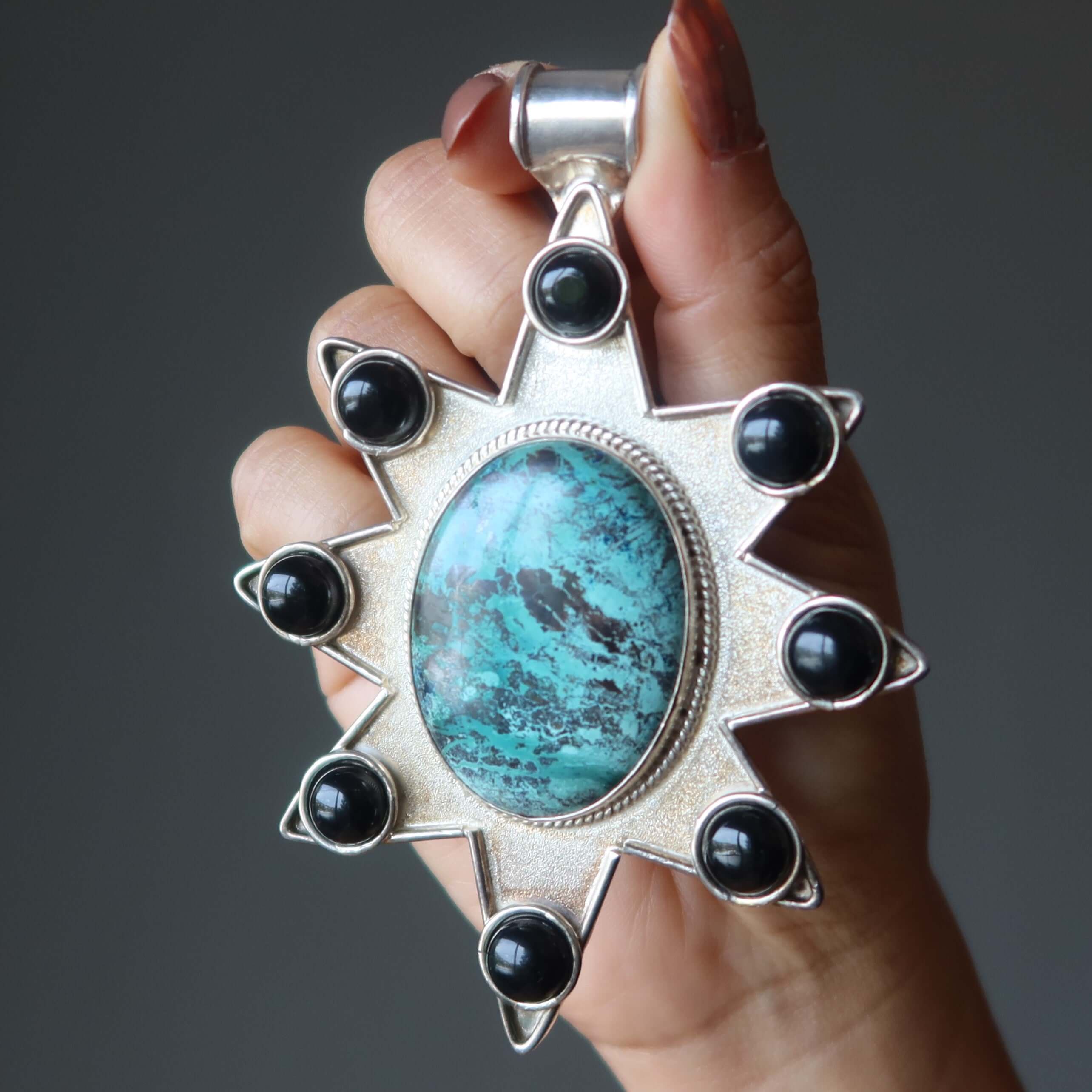Hand holding sterling silver Chrysocolla pendant with large oval Chrysocolla stone in 8-pointed star design