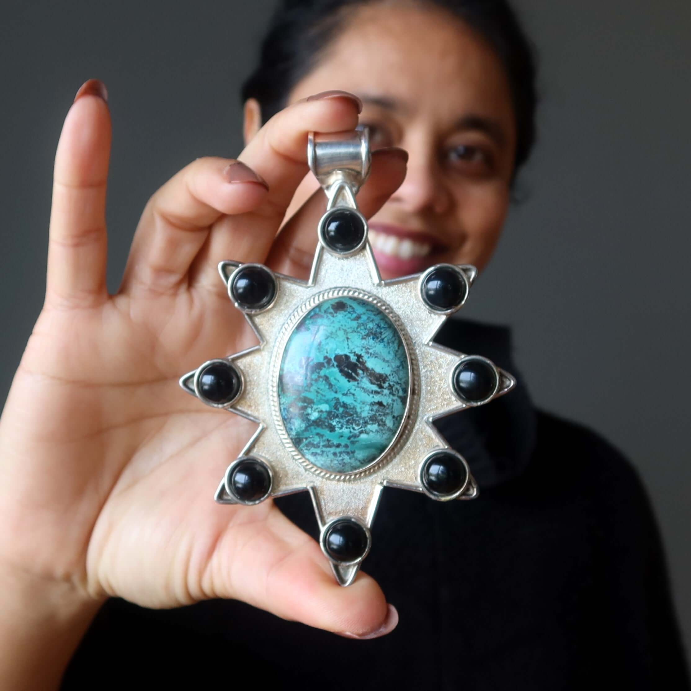 Woman holding large sterling silver Chrysocolla star pendant with black accent stones close to the camera