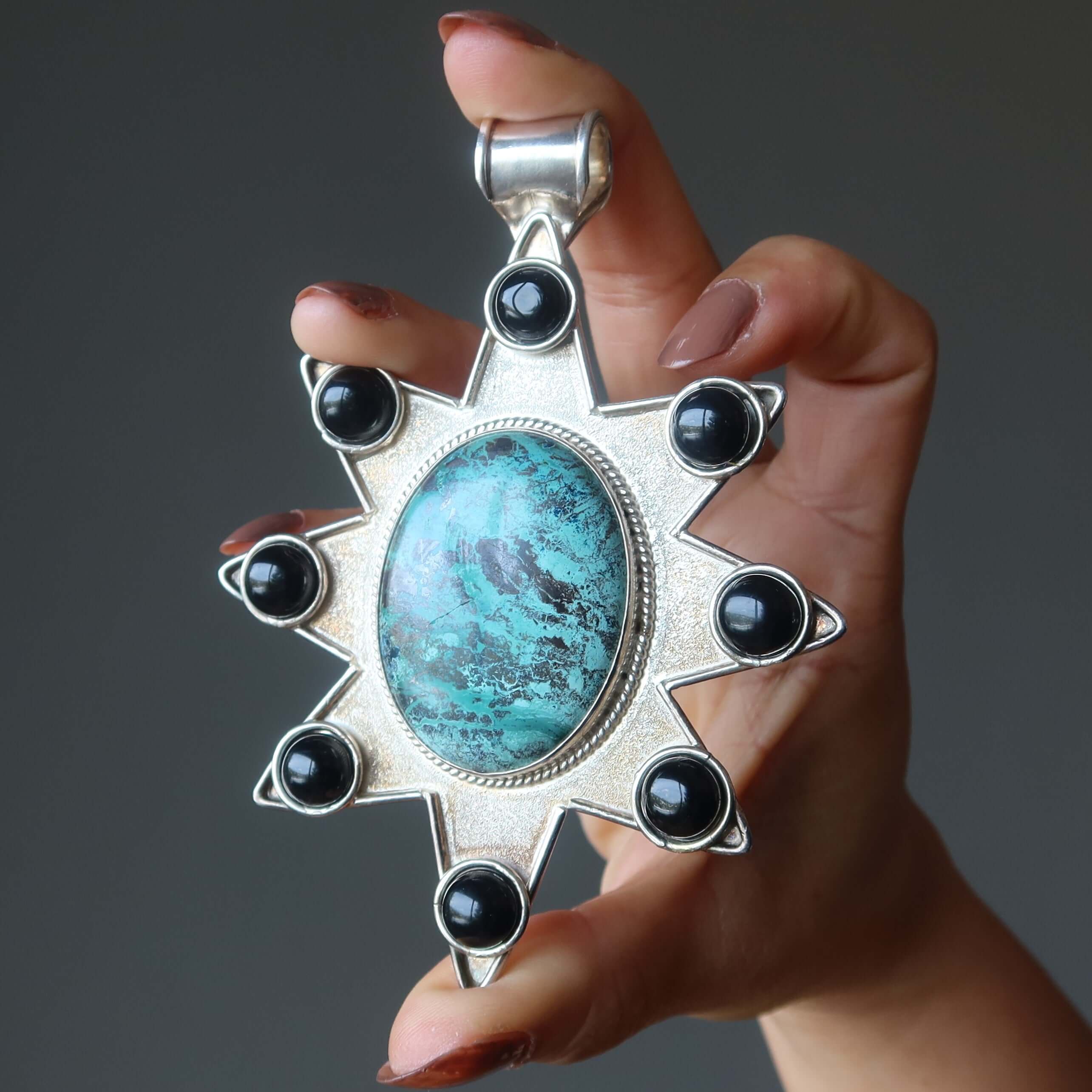 Hand holding sterling silver Chrysocolla star pendant with large oval gemstone and black accents