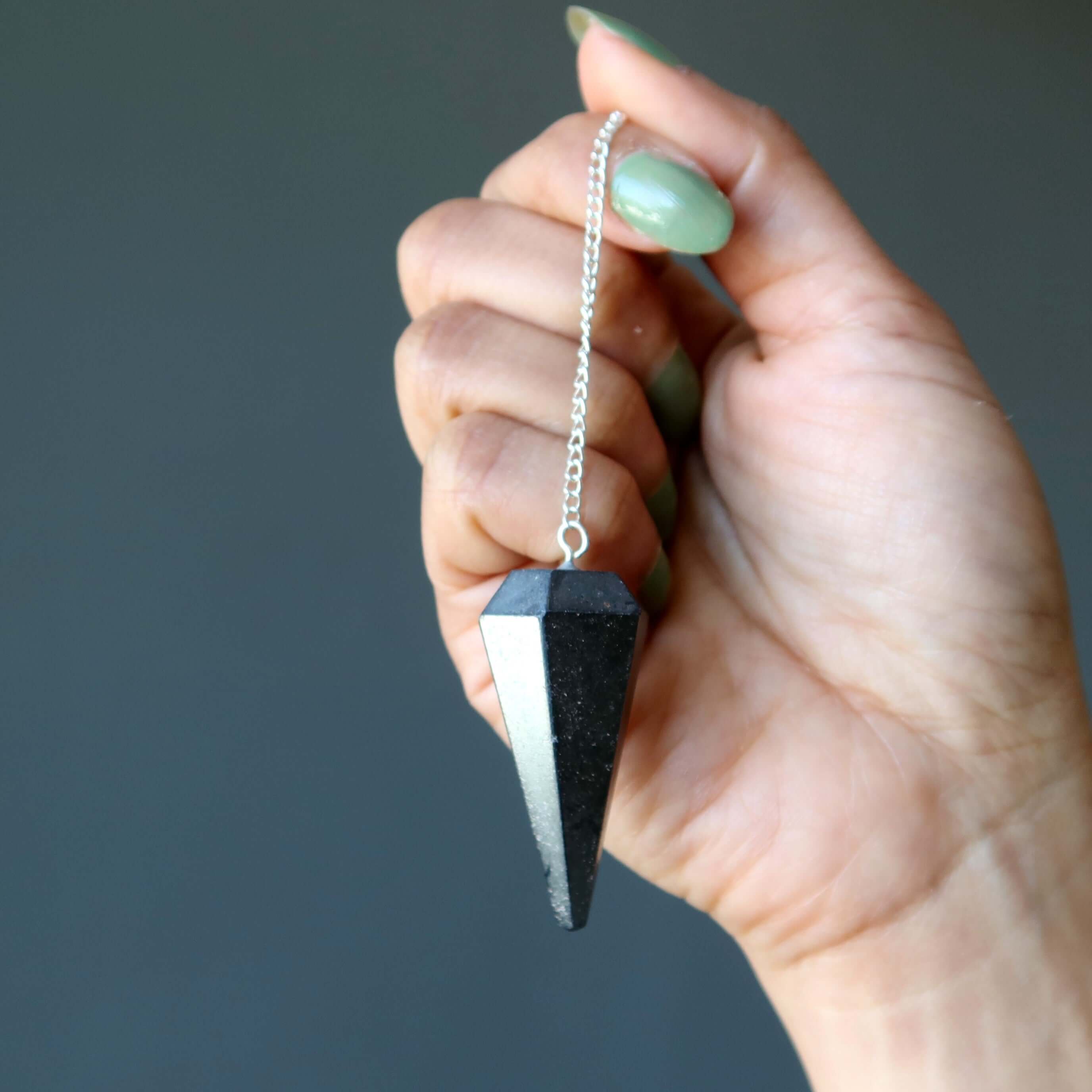 Hematite pendulum dowsing stone of truth held by hand for spiritual healing and grounding