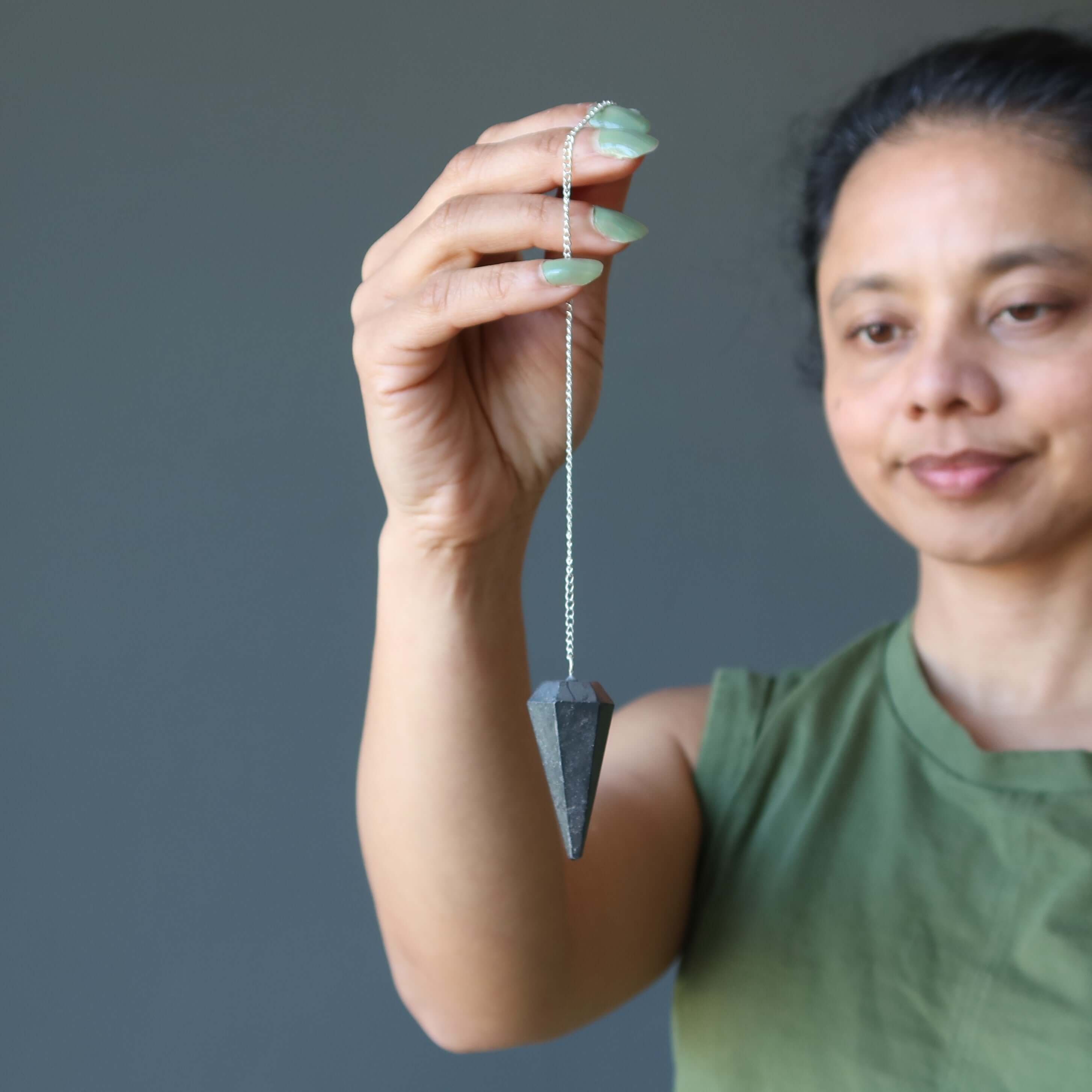 Woman holding Hematite pendulum dowsing stone of truth for spiritual healing and grounding