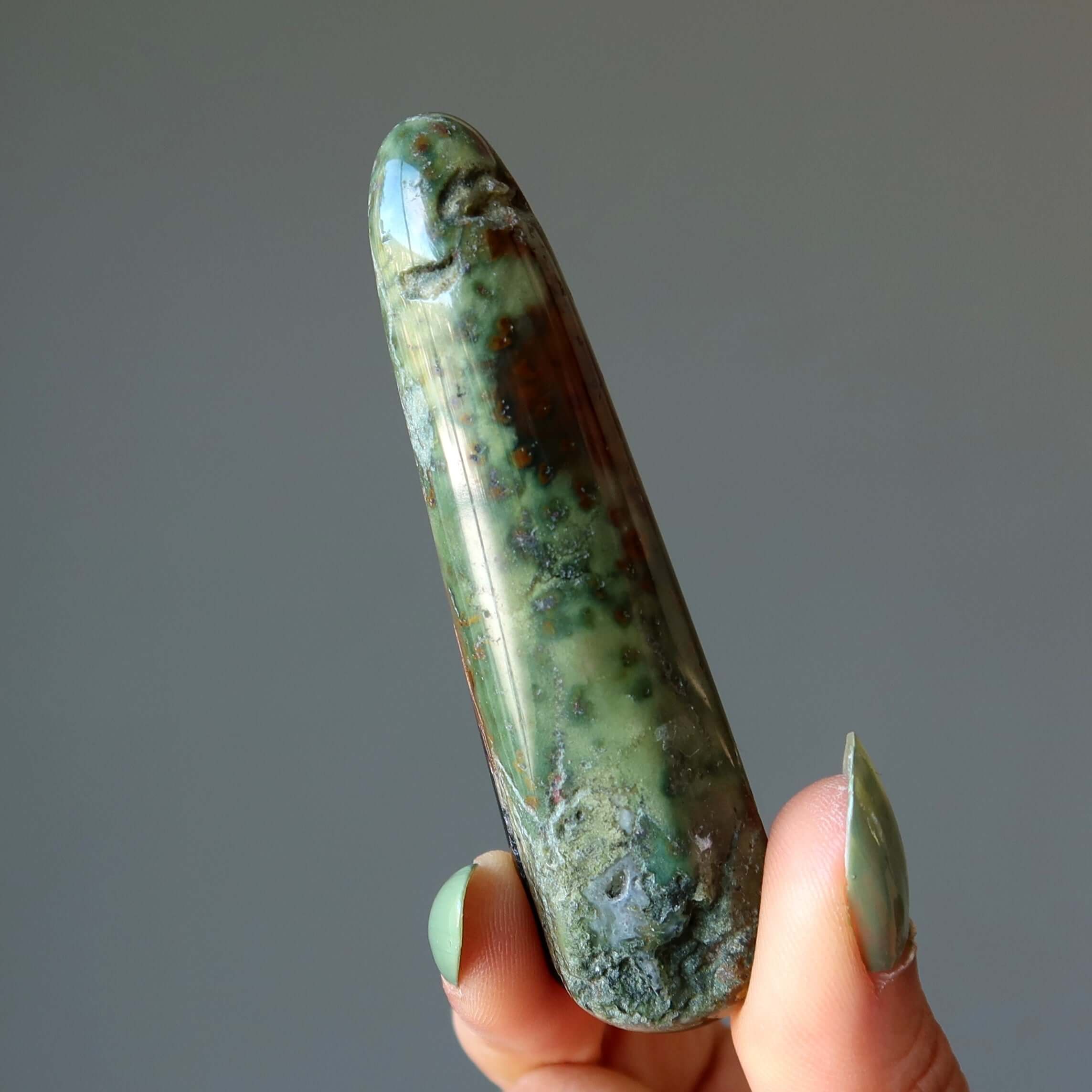 Hand holding polished green Jasper jasper massage wand crystal for grounding and stress relief