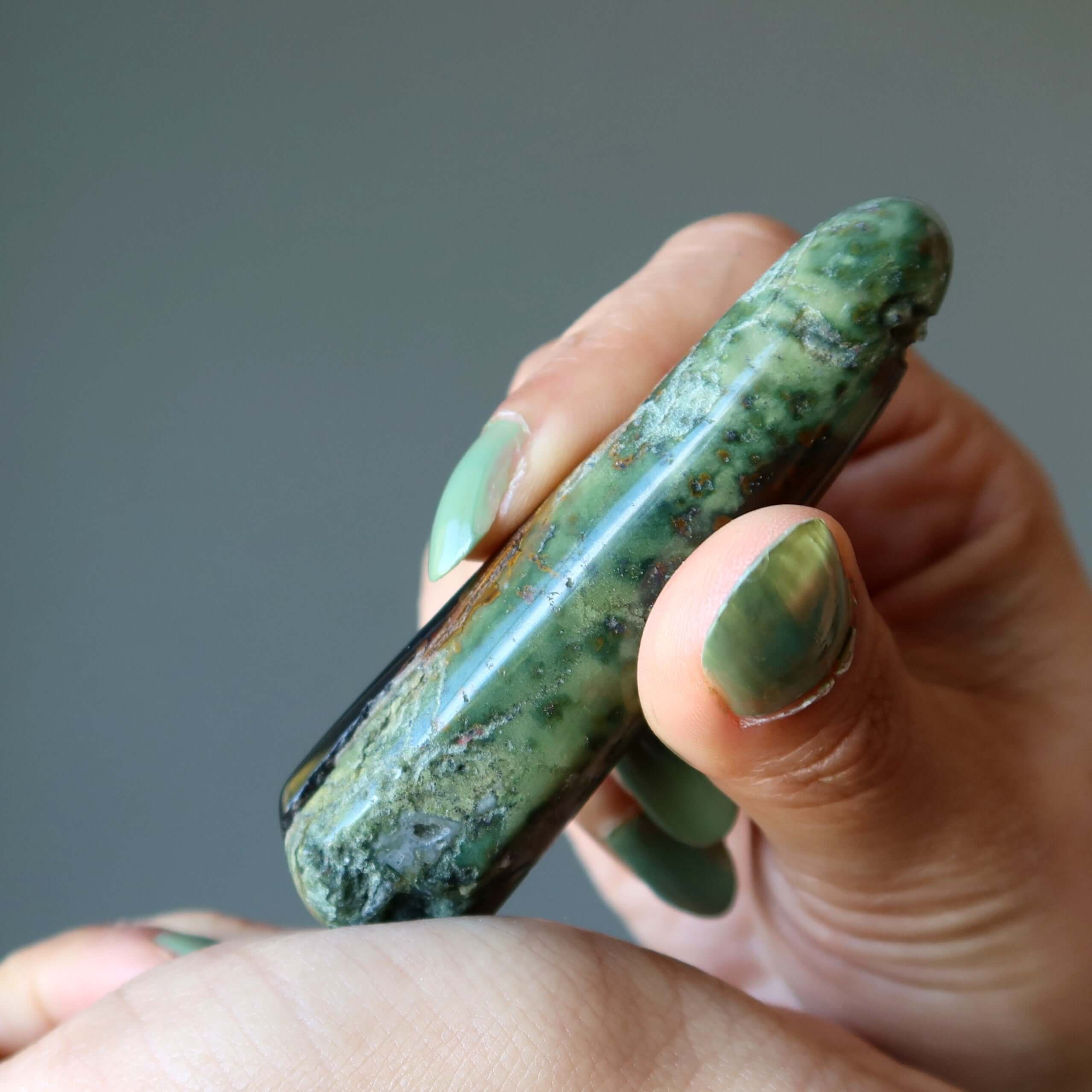 Hand holding polished green Jasper jasper massage wand for grounding massage and crystal healing