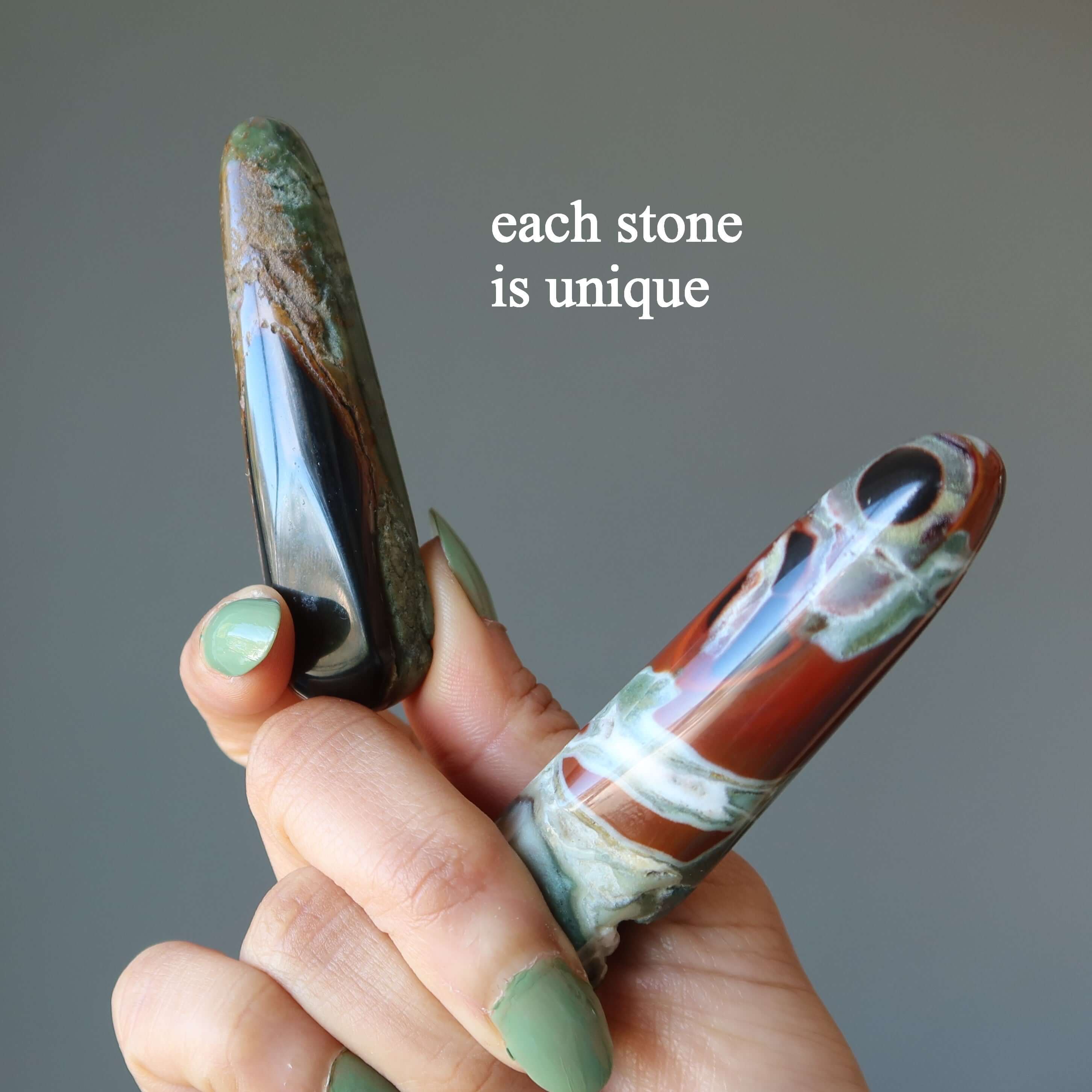 Hand holding two Jasper jasper massage wand stones showing unique earthy colors and patterns