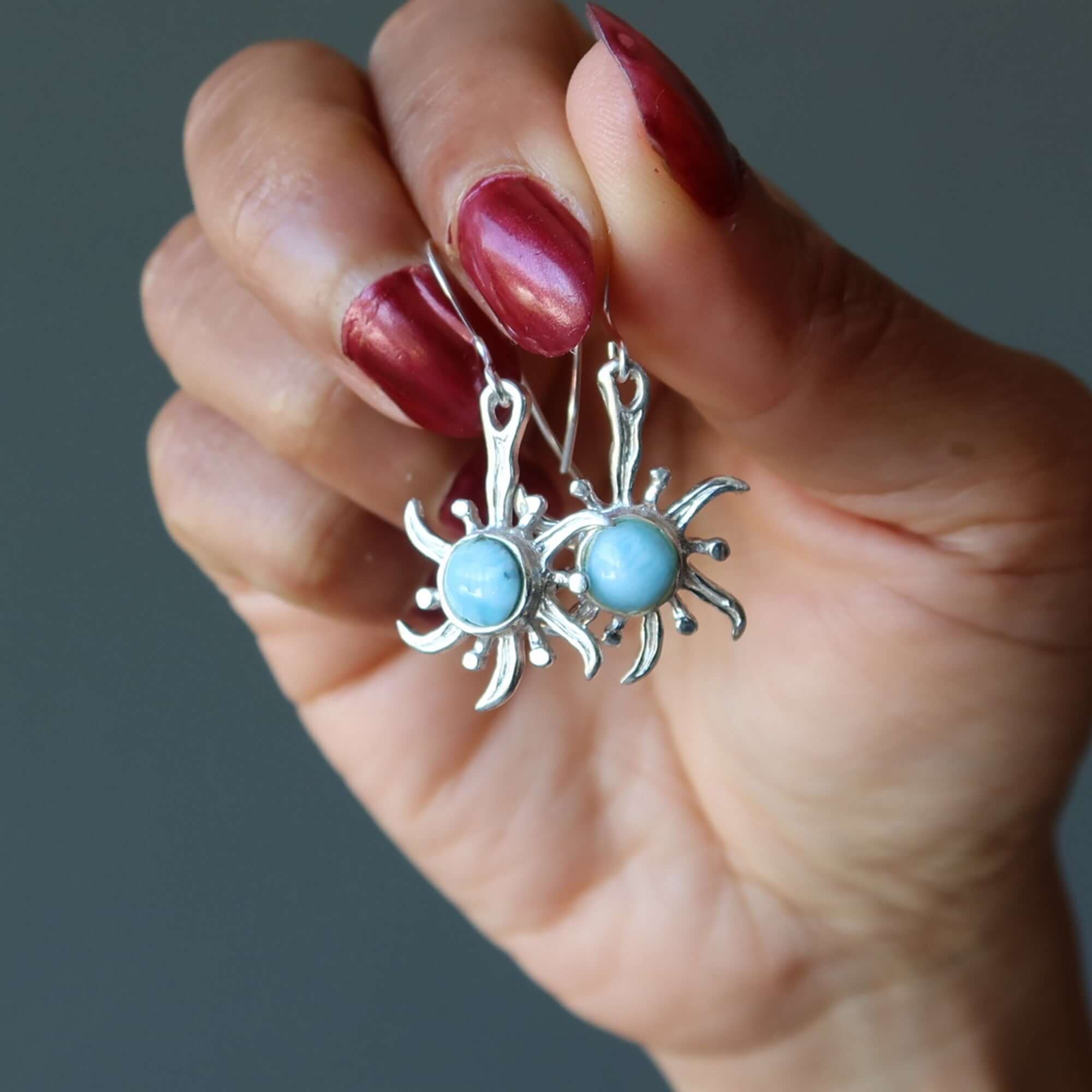 Larimar sterling silver sun earrings with blue gemstones held in hand