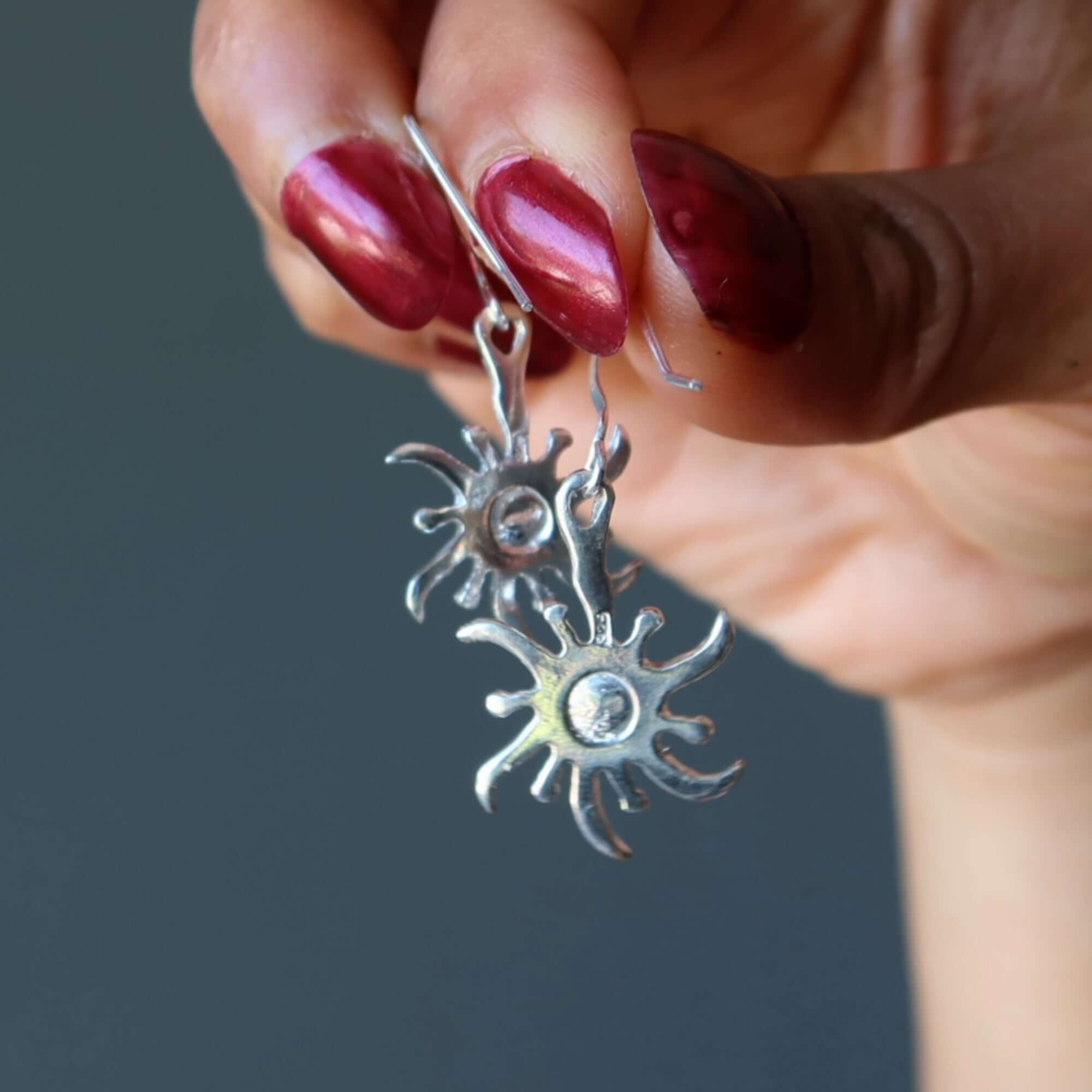 Larimar sterling silver sun earrings with blue gemstone centers held between fingers