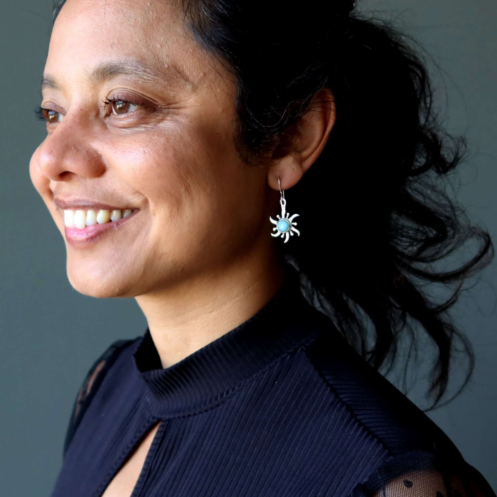 Woman smiling in black top wearing Larimar sun earrings in sterling silver