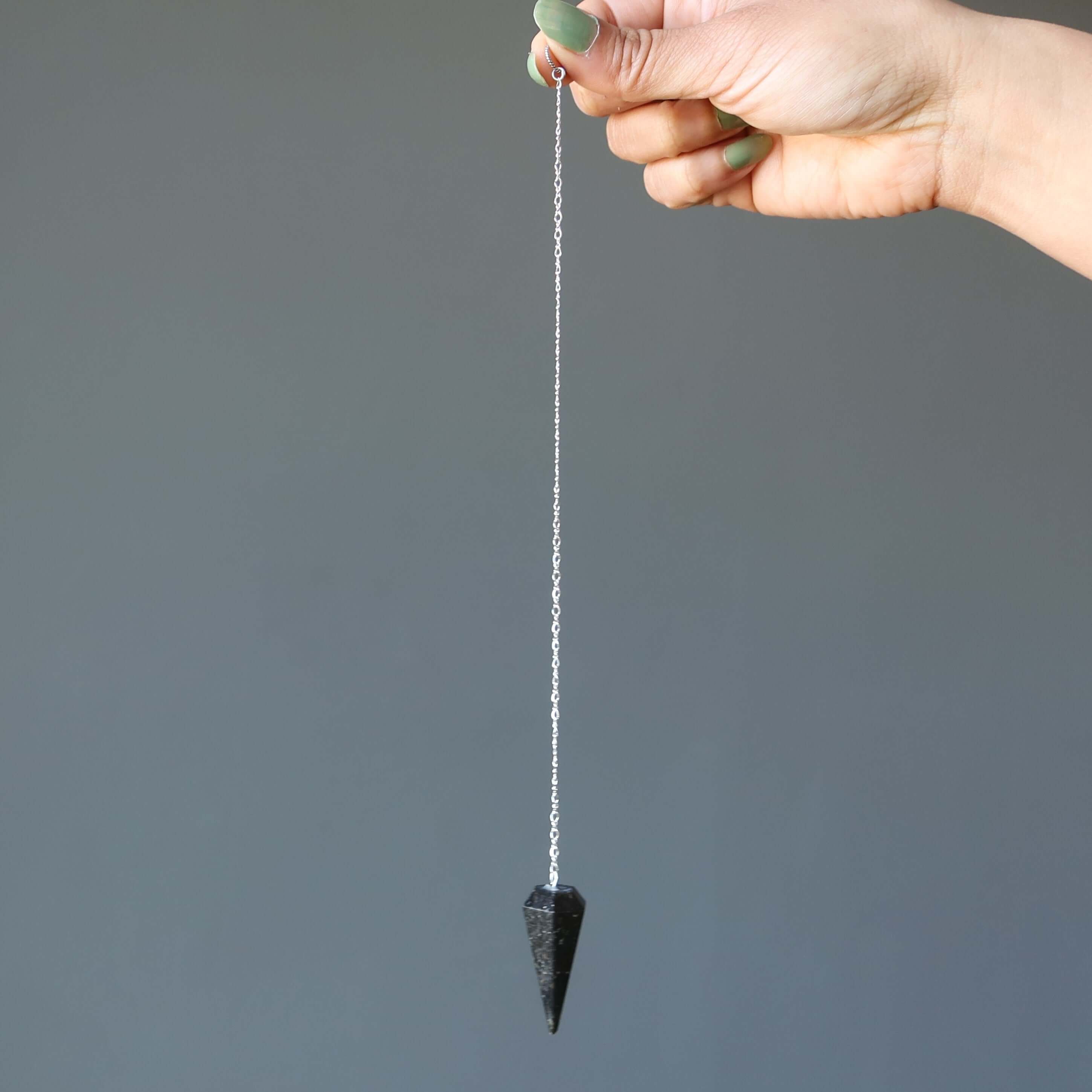 Hand holding Nuummite Pendulum Mysteries sterling silver Pendulum for dowsing and chakra healing