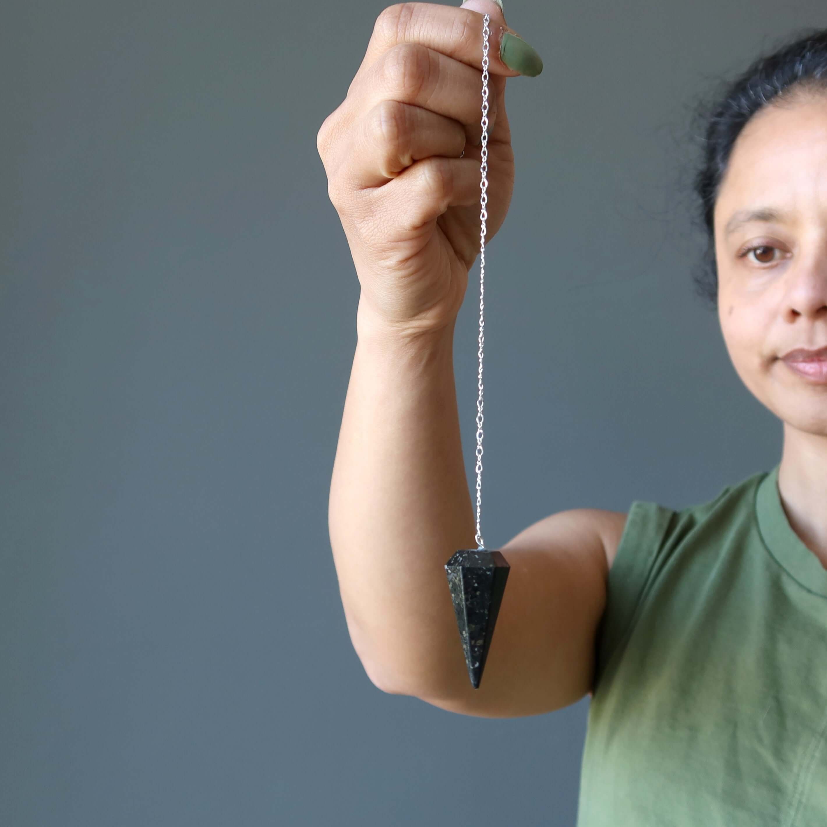 Woman holding Nuummite Pendulum Mysteries sterling silver Pendulum for dowsing, healing, and chakra assessment