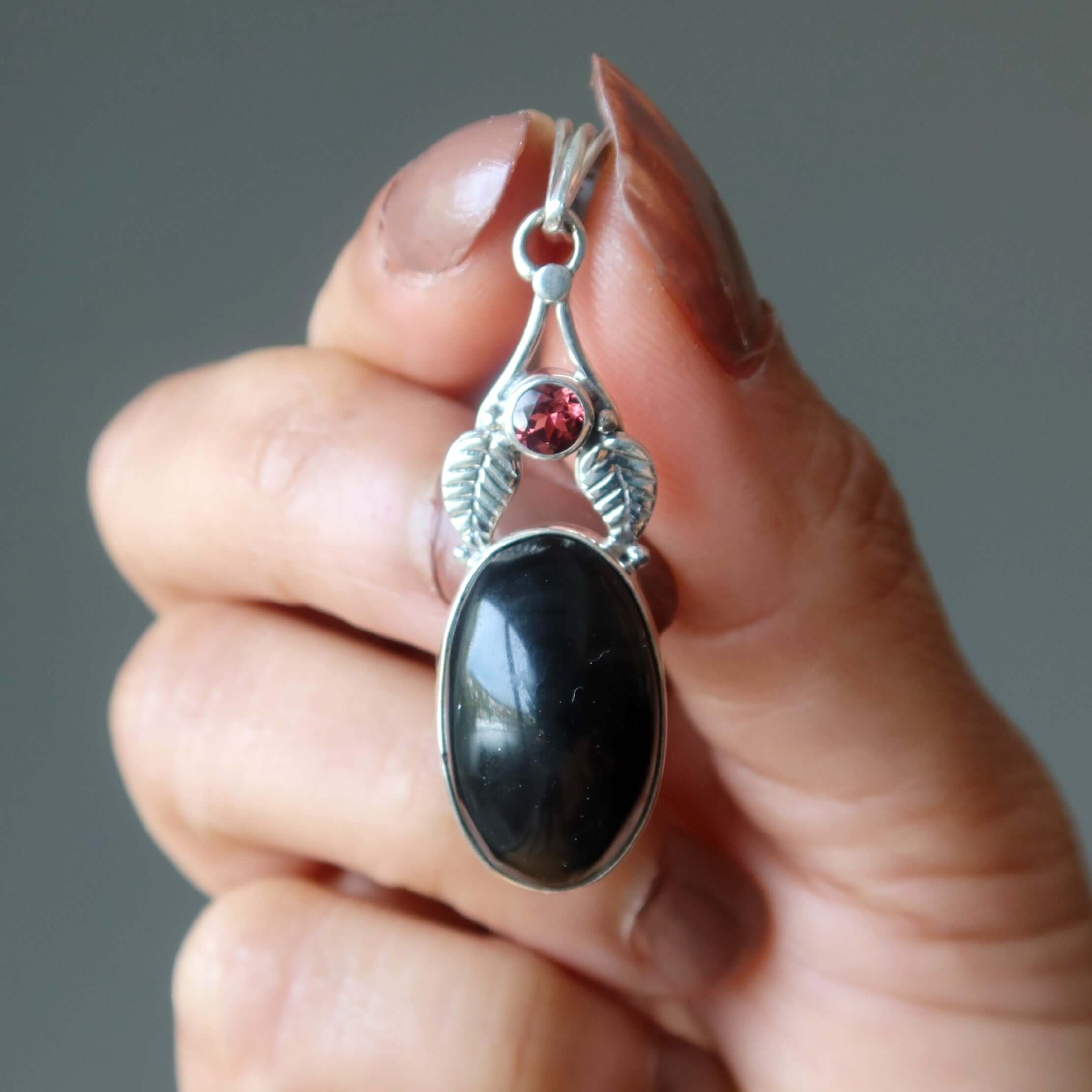 Rainbow Obsidian pendant bodyguard in sterling silver with garnet accent held between fingers