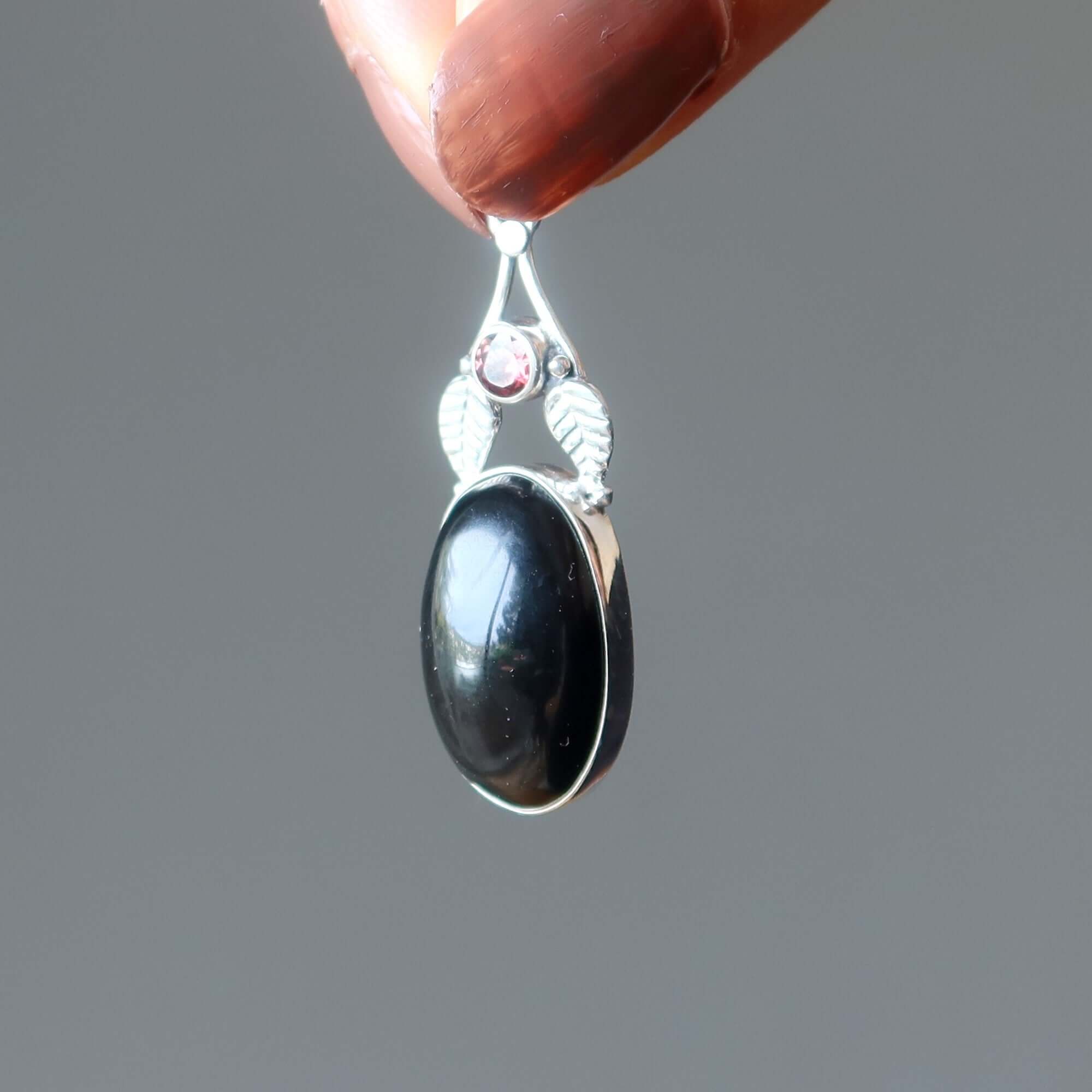 Rainbow Obsidian pendant bodyguard in sterling silver with garnet accent held up to light