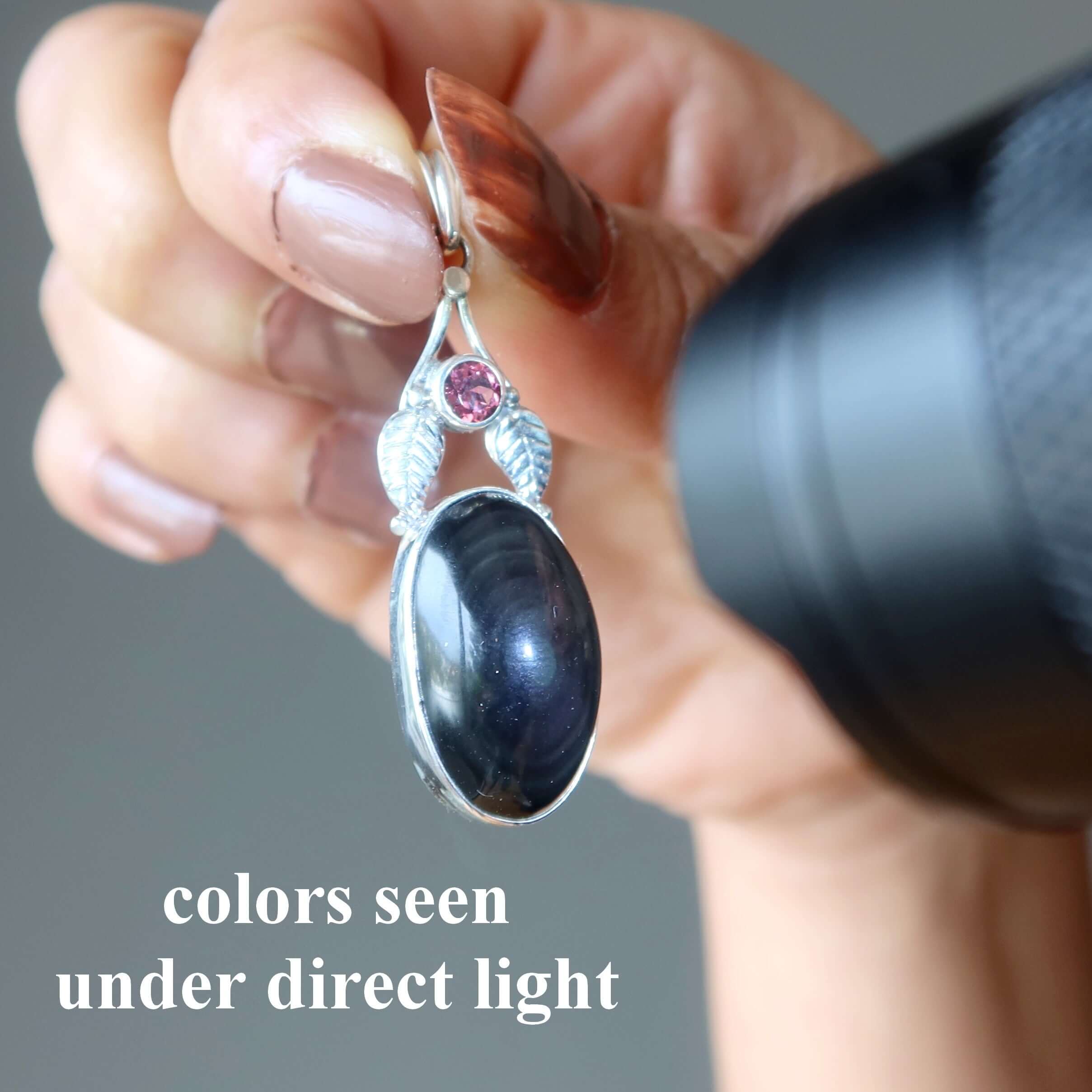 Rainbow Obsidian Pendant Bodyguard Sterling Silver with garnet accent shown under direct light in hand