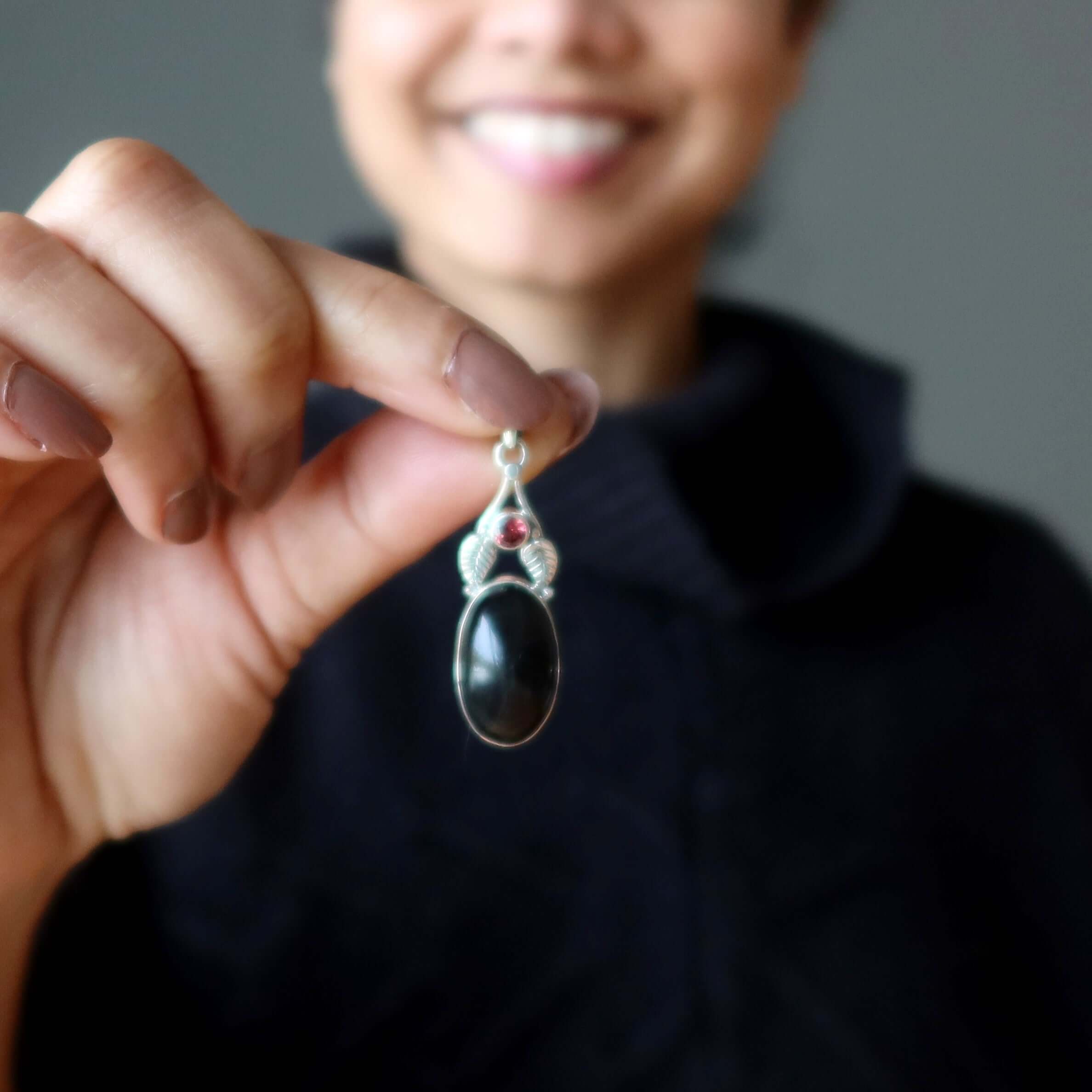 Woman holding Rainbow Obsidian Pendant Bodyguard in sterling silver with garnet accent close to the camera