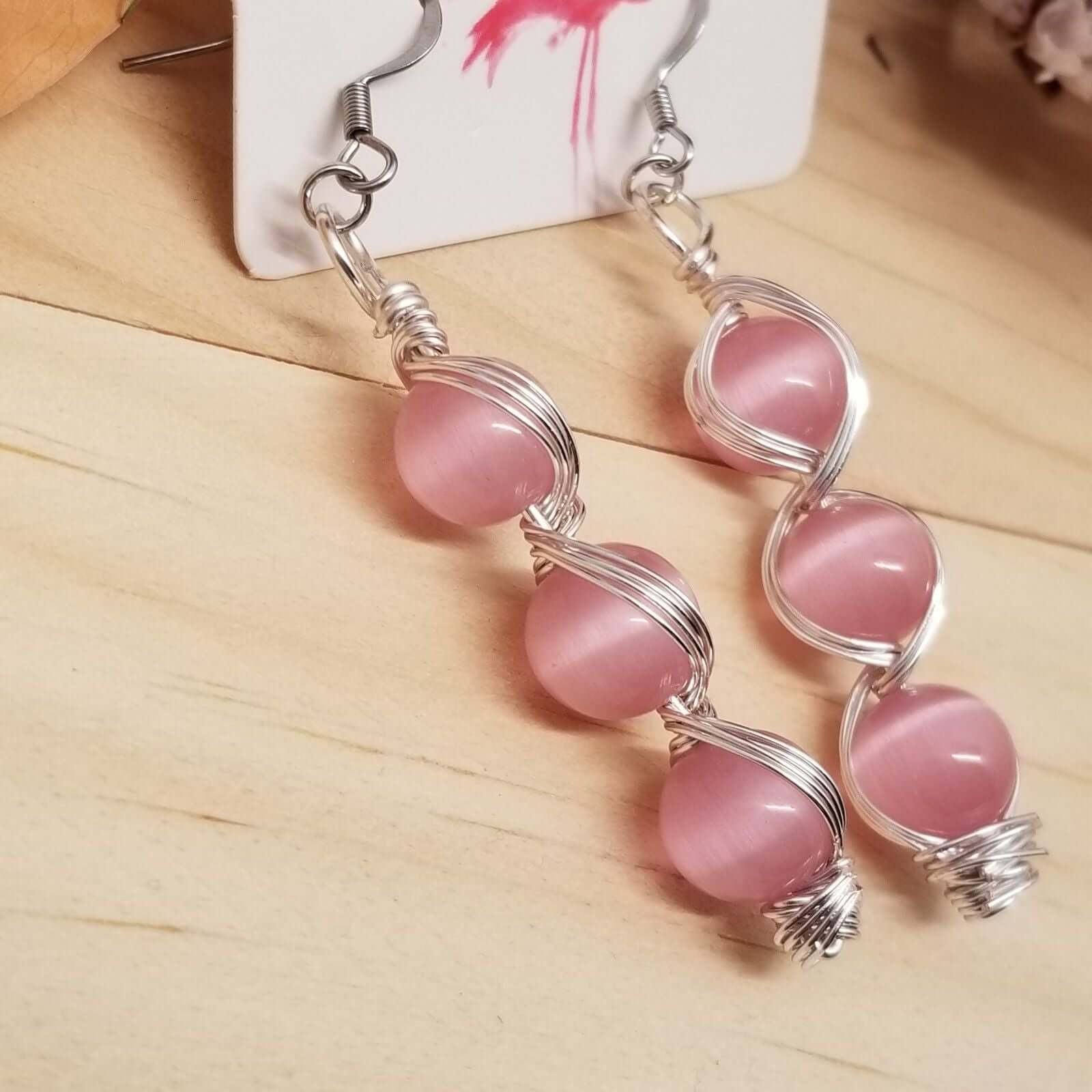 Handmade Pink Cat’s Eye Bead Earrings – Wire Wrapped Dangle Jewelry with stacked pink beads and silver-tone wire on wood background
