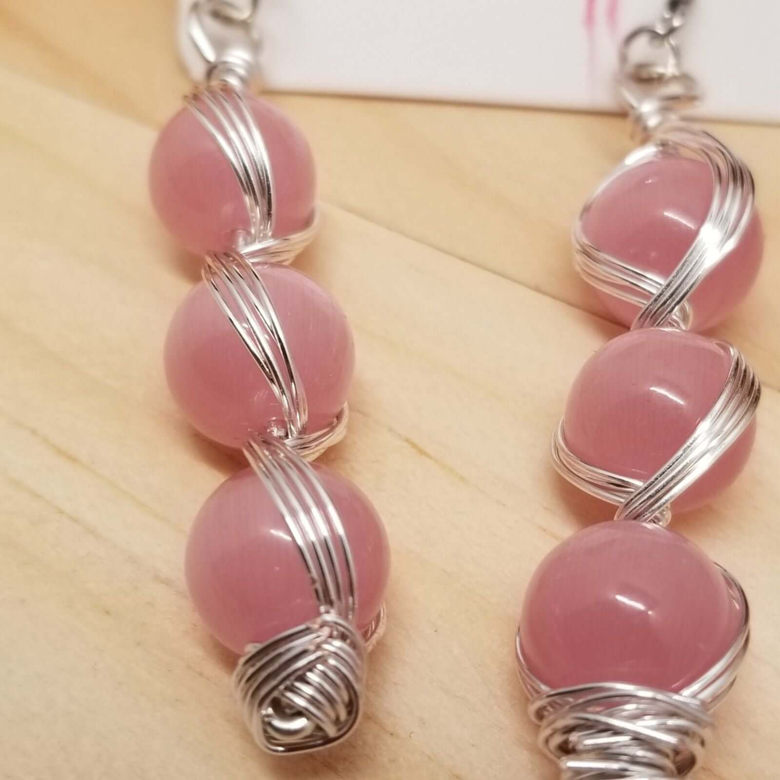 Handmade Pink Cat’s Eye Bead Earrings – Wire Wrapped Dangle Jewelry with stacked pink beads and silver wire on wood background