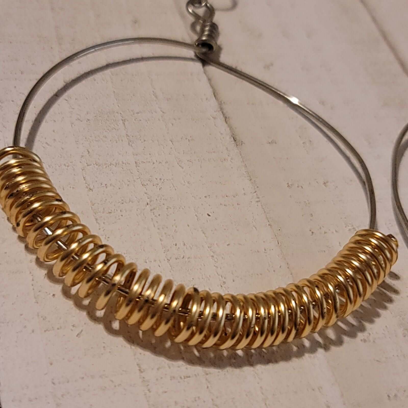 Handmade Gold Spring Hoop Earrings – Lightweight Wire Wrapped Hoops featuring silver-tone hoops with gold coil accents on rustic wood background