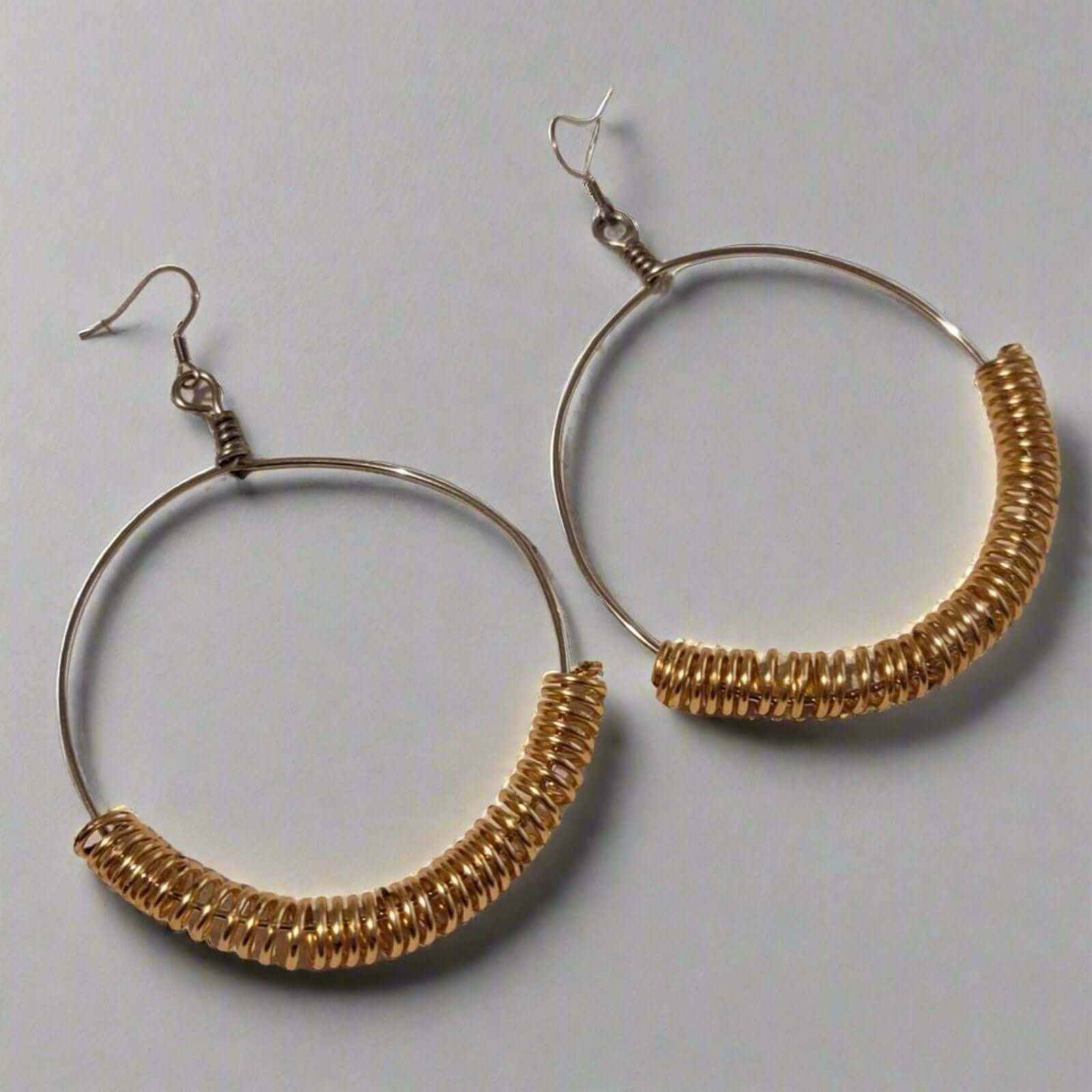Handmade Gold Spring Hoop Earrings – Lightweight Wire Wrapped Hoops with silver-tone base and gold coil detail on a gray background
