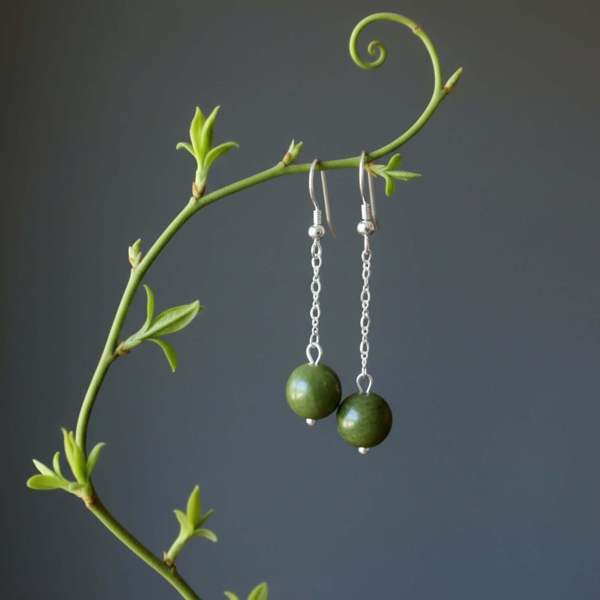 Serpentine green gemstone sterling silver dangle earrings hanging from a vine-like branch