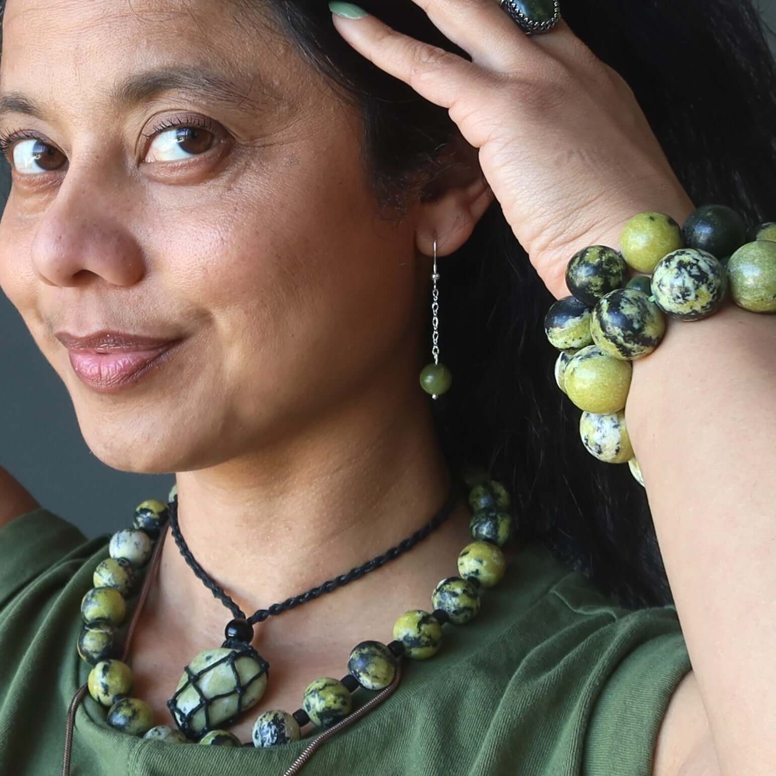 Woman wearing Serpentine earrings beyond time green sterling with matching green gemstone bracelet and necklace